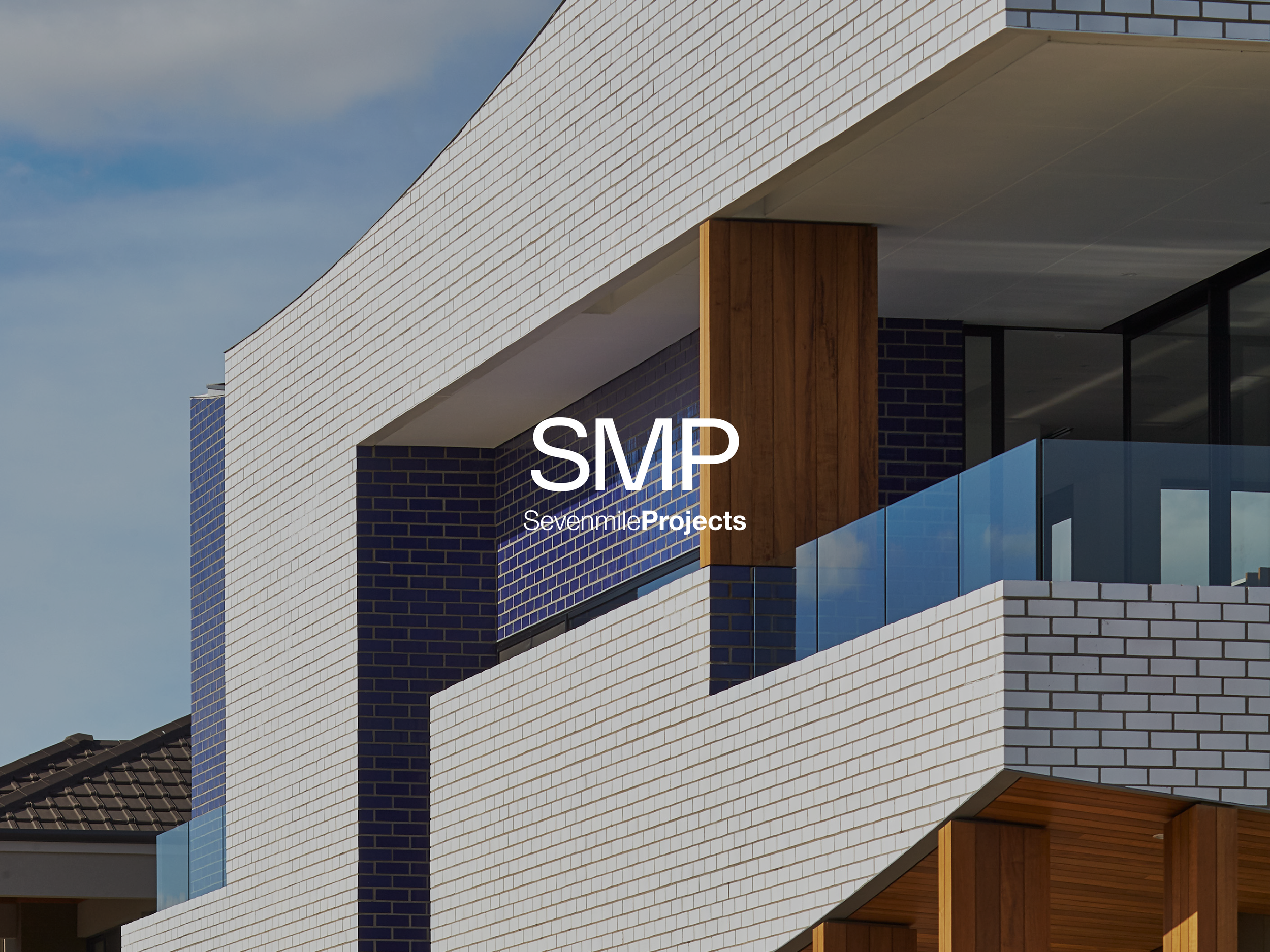 Close-up of a modern building with white brick facade, wood accents, and glass balcony railing, against a partly cloudy sky.