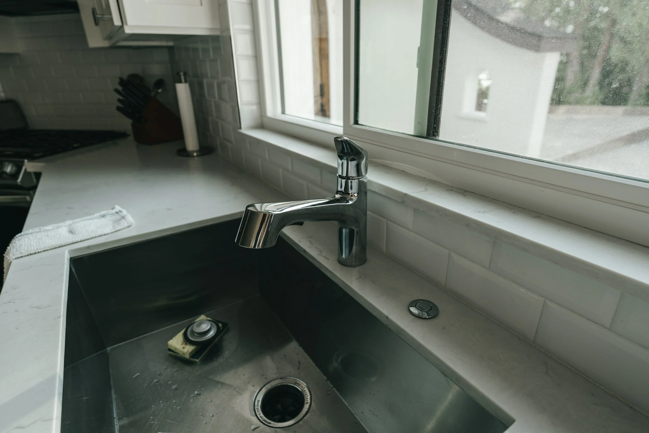 Kitchen sink with a chrome faucet, window above, and a soap dish with soap in the sink.