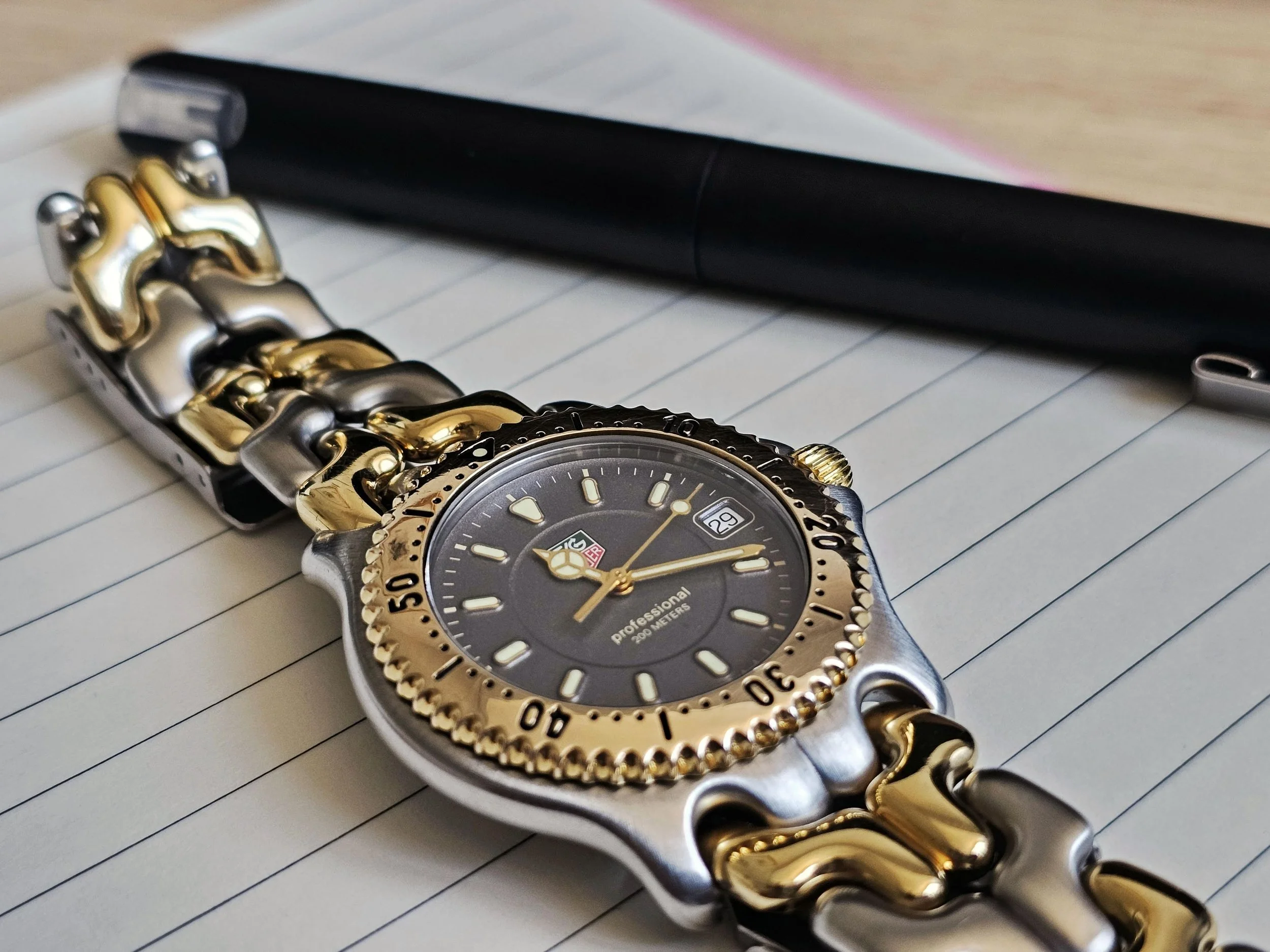 Une montre TAG Heuer posé sur un carnet à côté d'un stylo