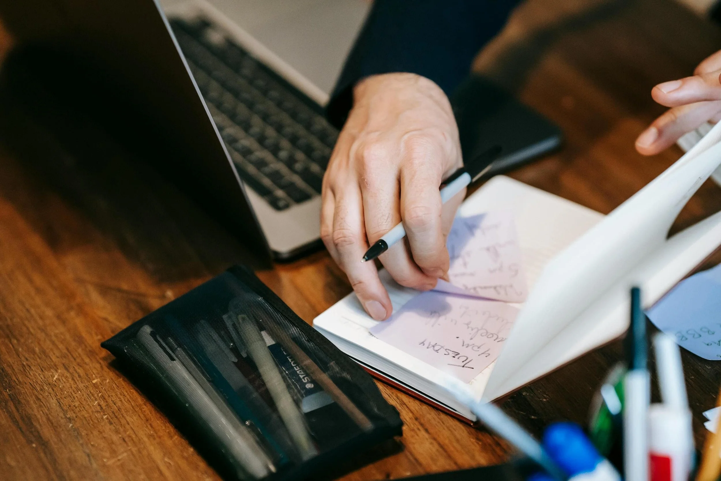 Une personne écrit sur un carnet devant son PC