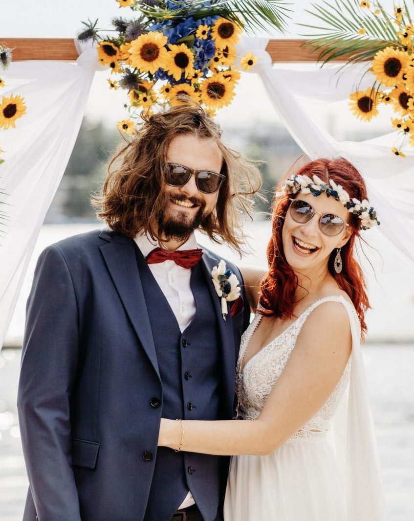 Ein cooles Hochzeitspaar breit lächelnd vor Sonnenblumen