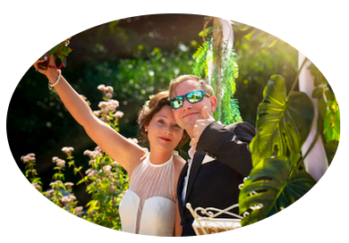 Ein Hochzeitspaar vor Ulrike hebt freudig triumphierend jeweils den Arm hoch der Bräutigam trägt eine Sonnenbrille