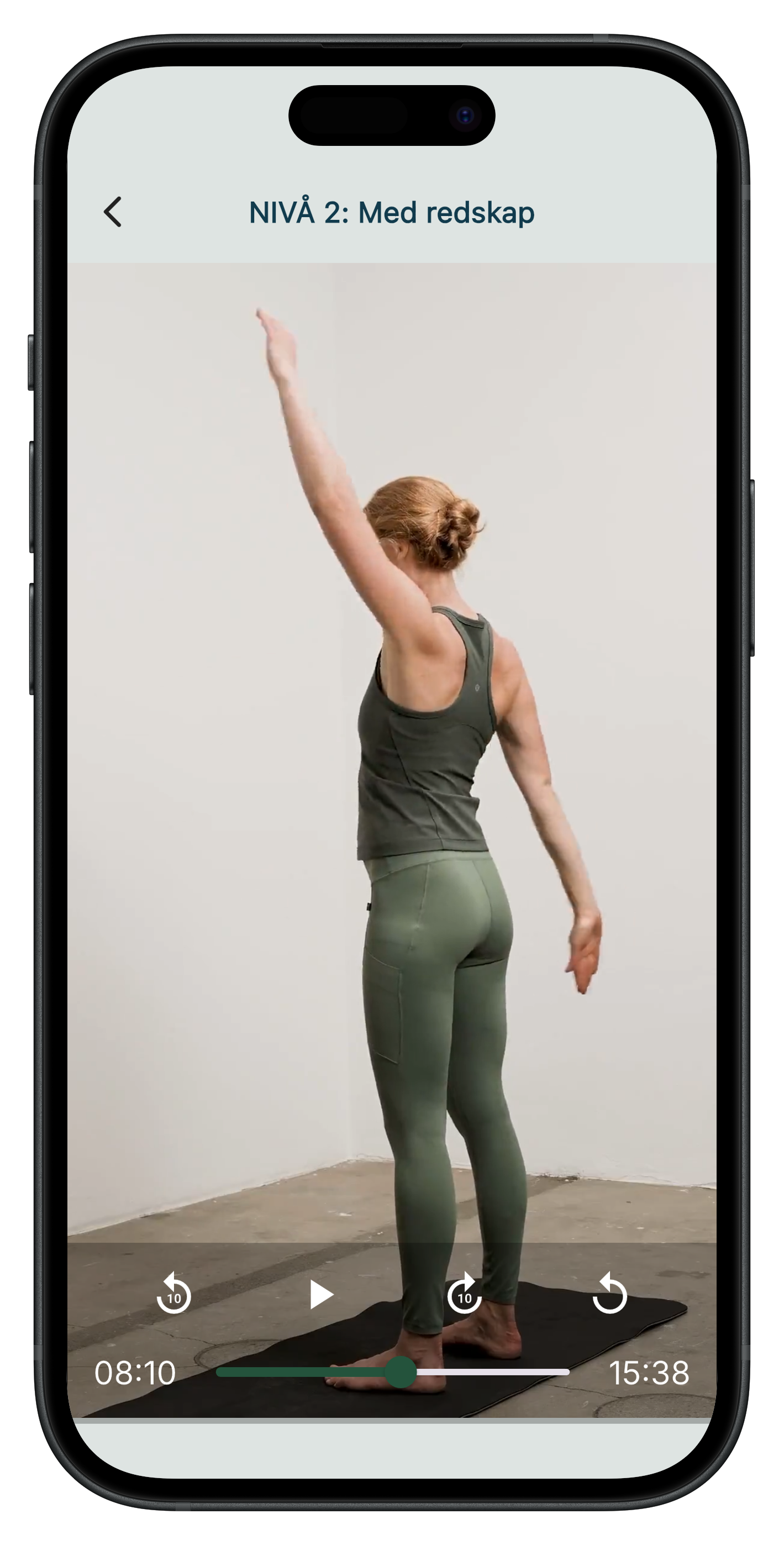 En kvinna med rött hår som utför ryggträning på en svart matta, bakom en vit vägg.