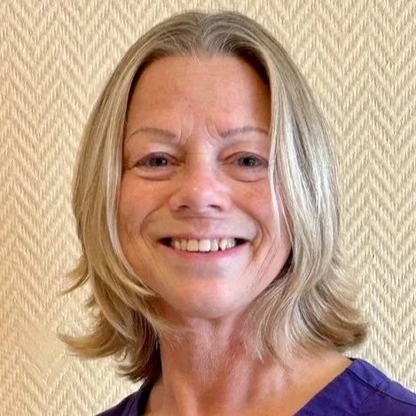 En kvinna med axellångt blond hår, leende, mot en beige vägg med mönster, som använder osteoporosgymmet