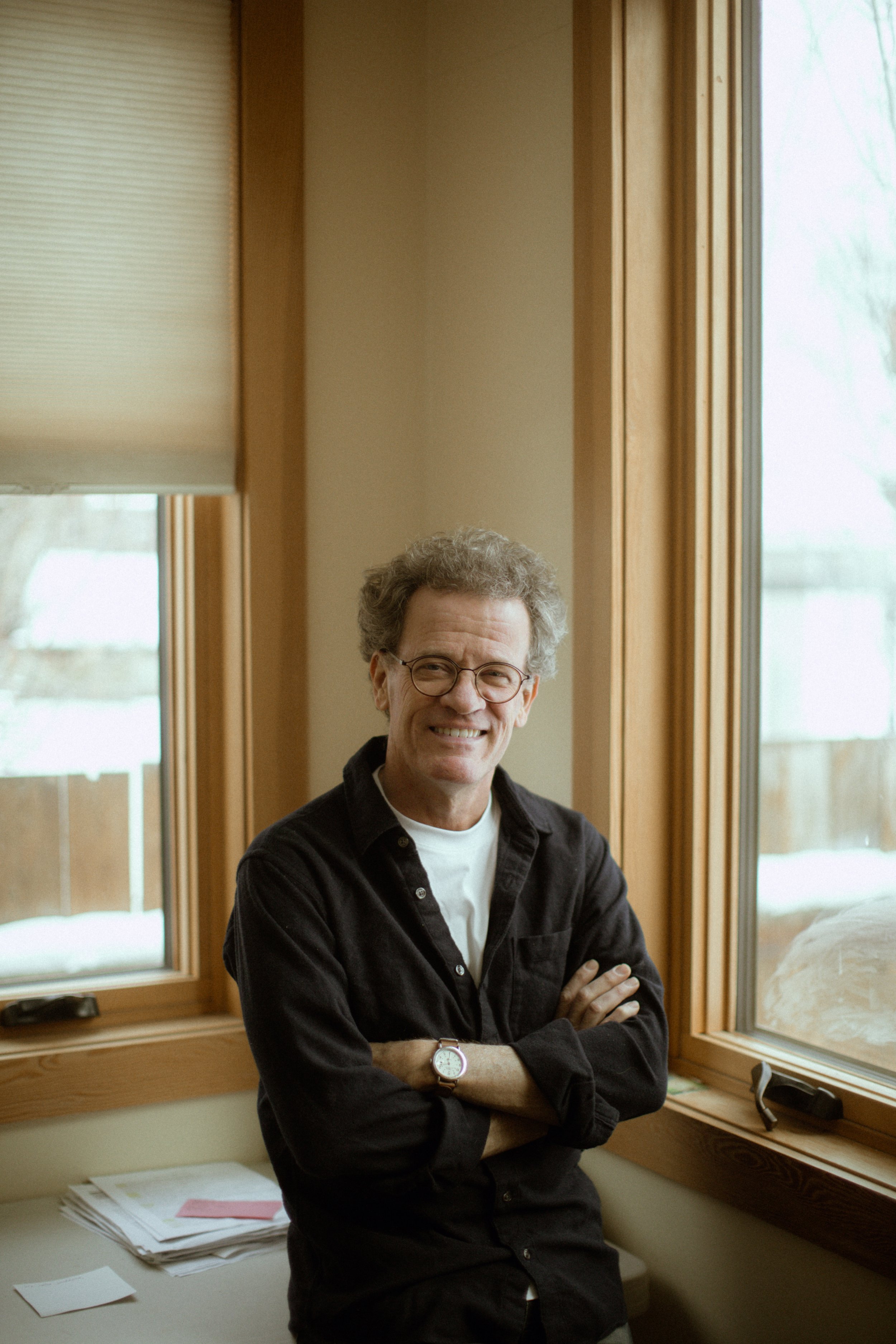Yann Martel smiling with arms crossed indoors by window