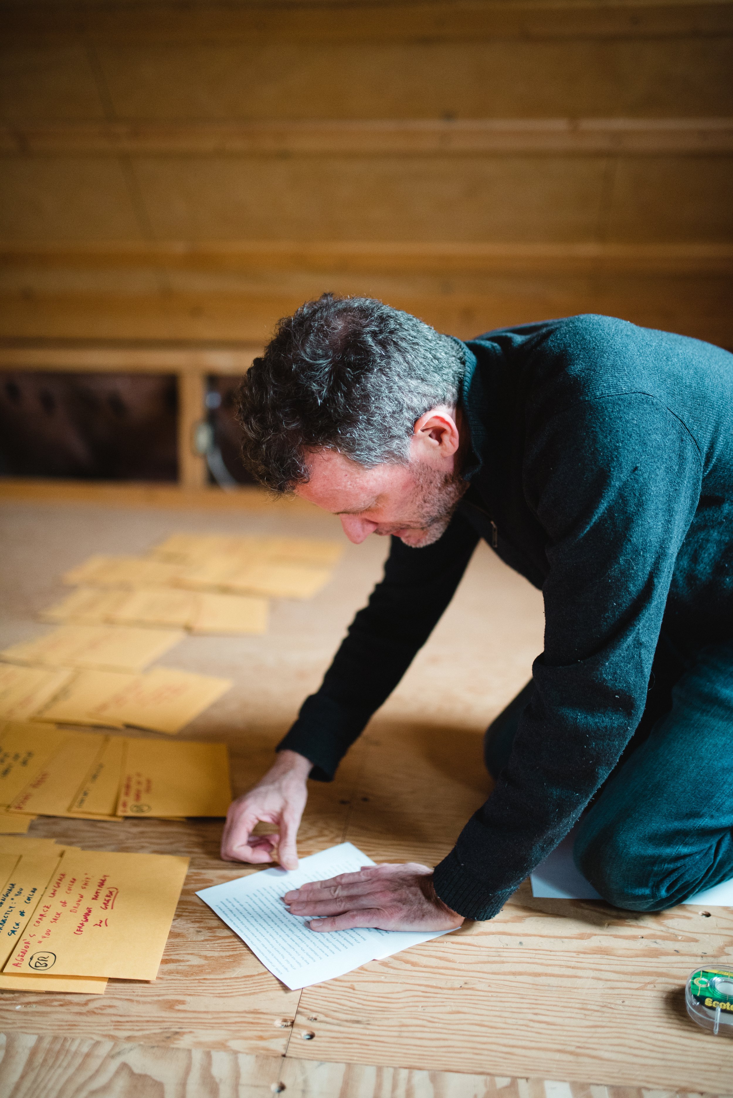 Yann Martel kneeling on the floor arranging pages and envelopes