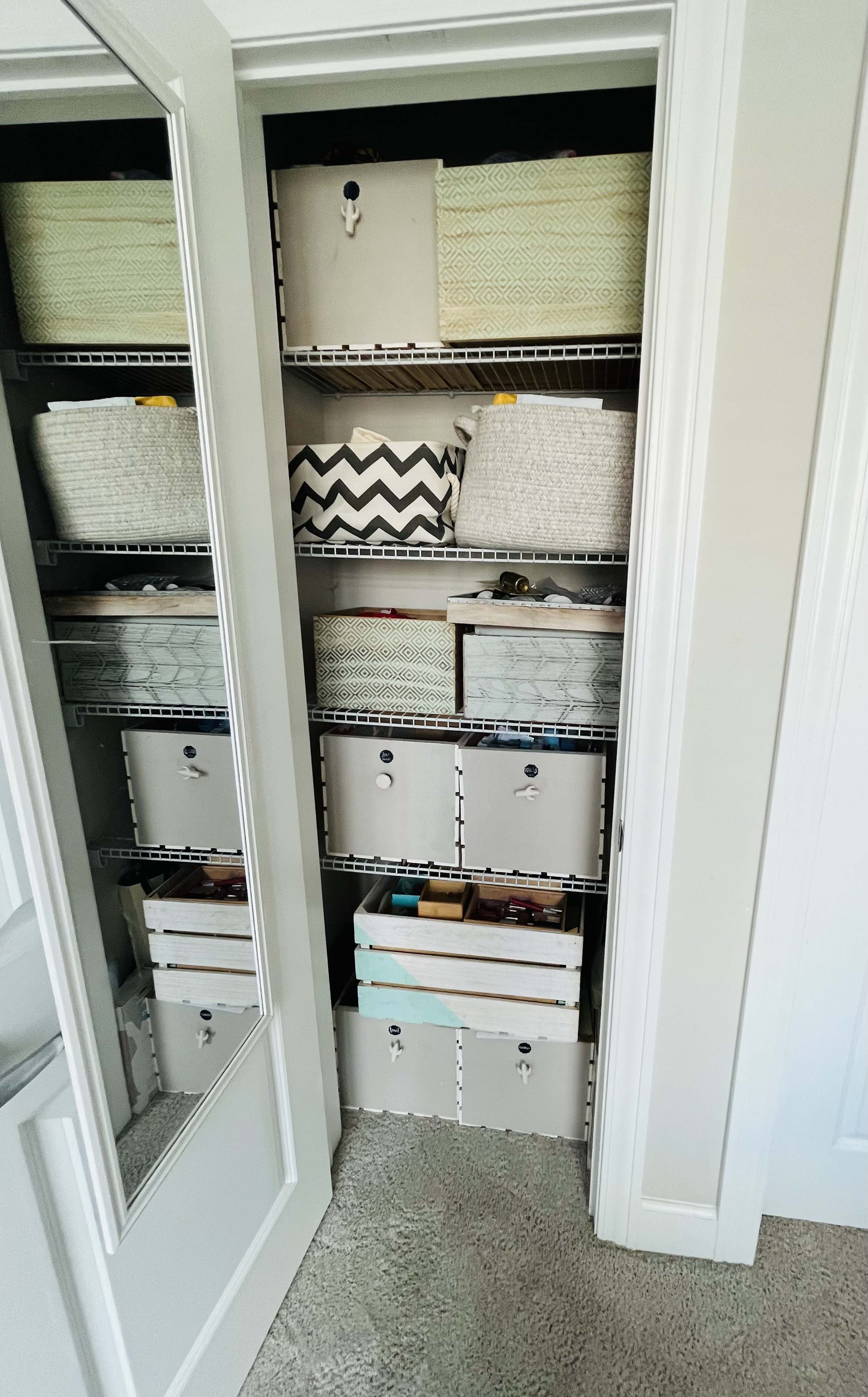 A closet with open doors revealing organized storage in white, gray, and beige containers and baskets on open shelves.