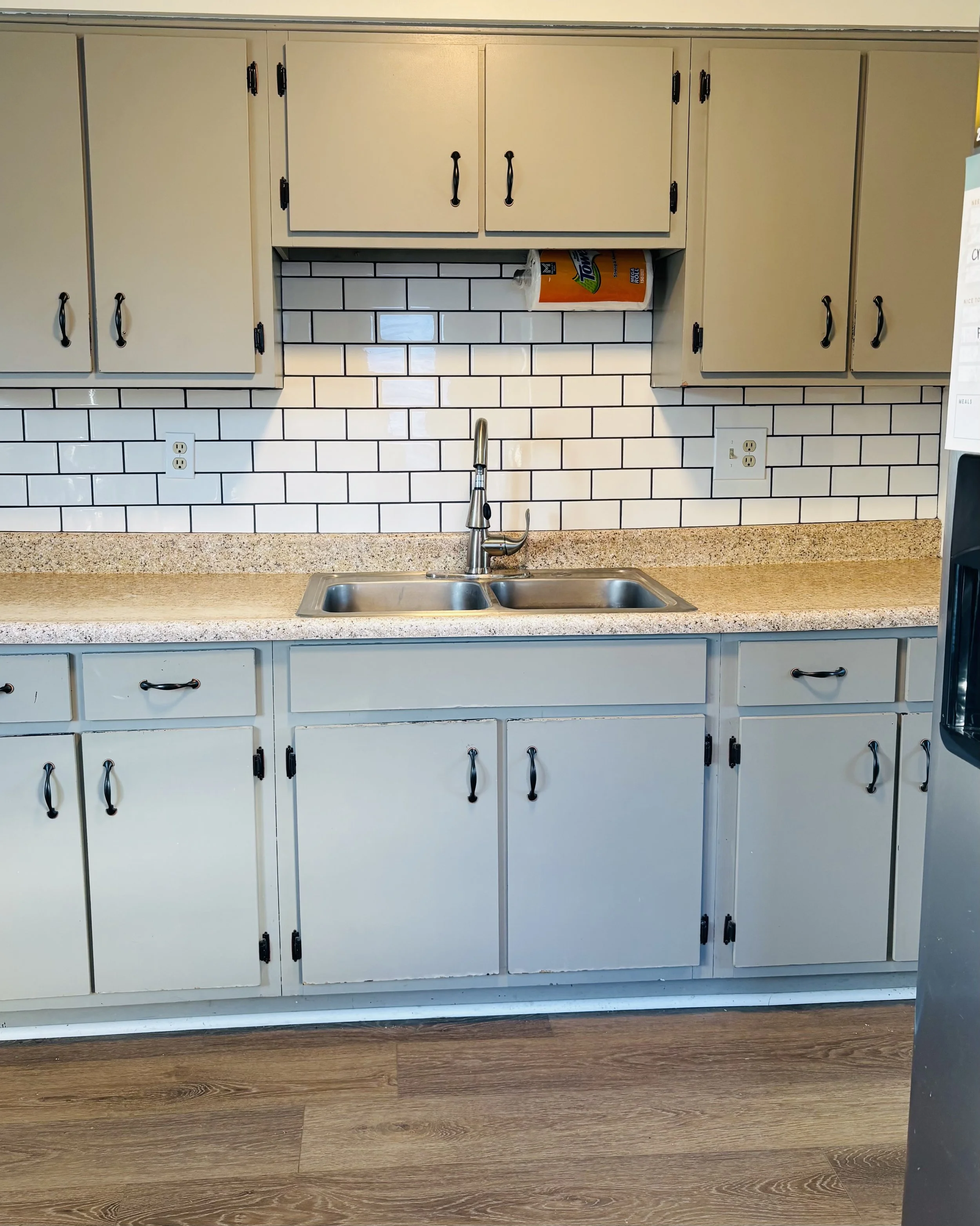 Kitchen with beige cabinets, white subway tile backsplash, double sink, and paper towel roll above the sink.