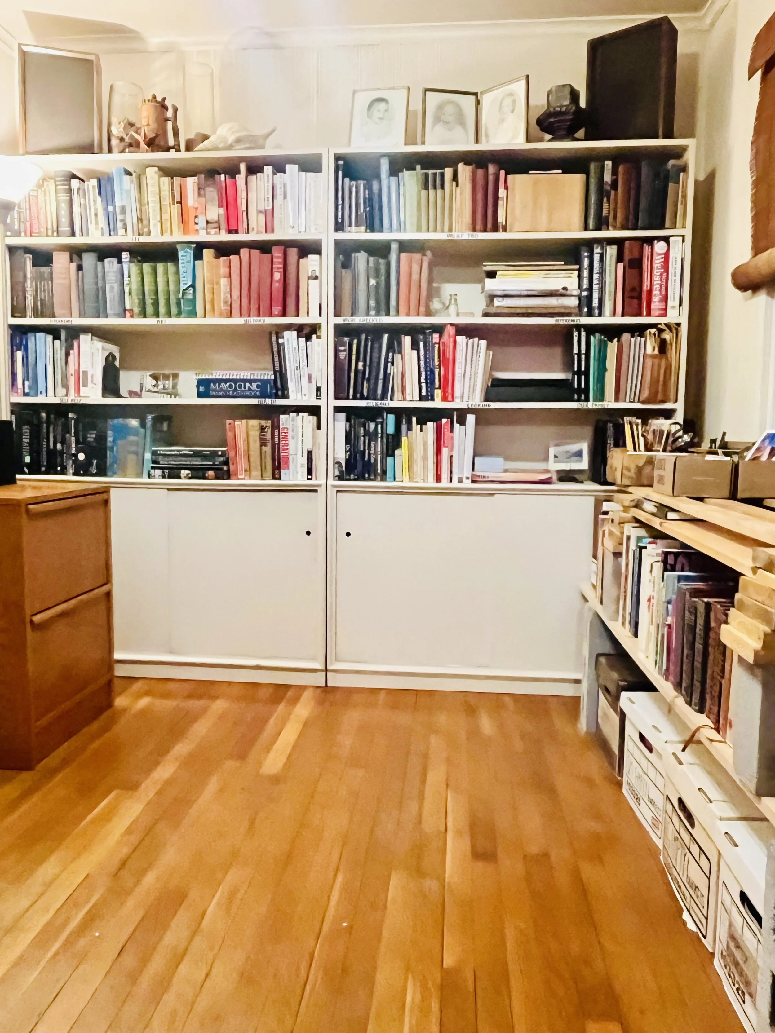 Bookshelves filled with books, photos, and decorative items in a cozy room with wooden floors.