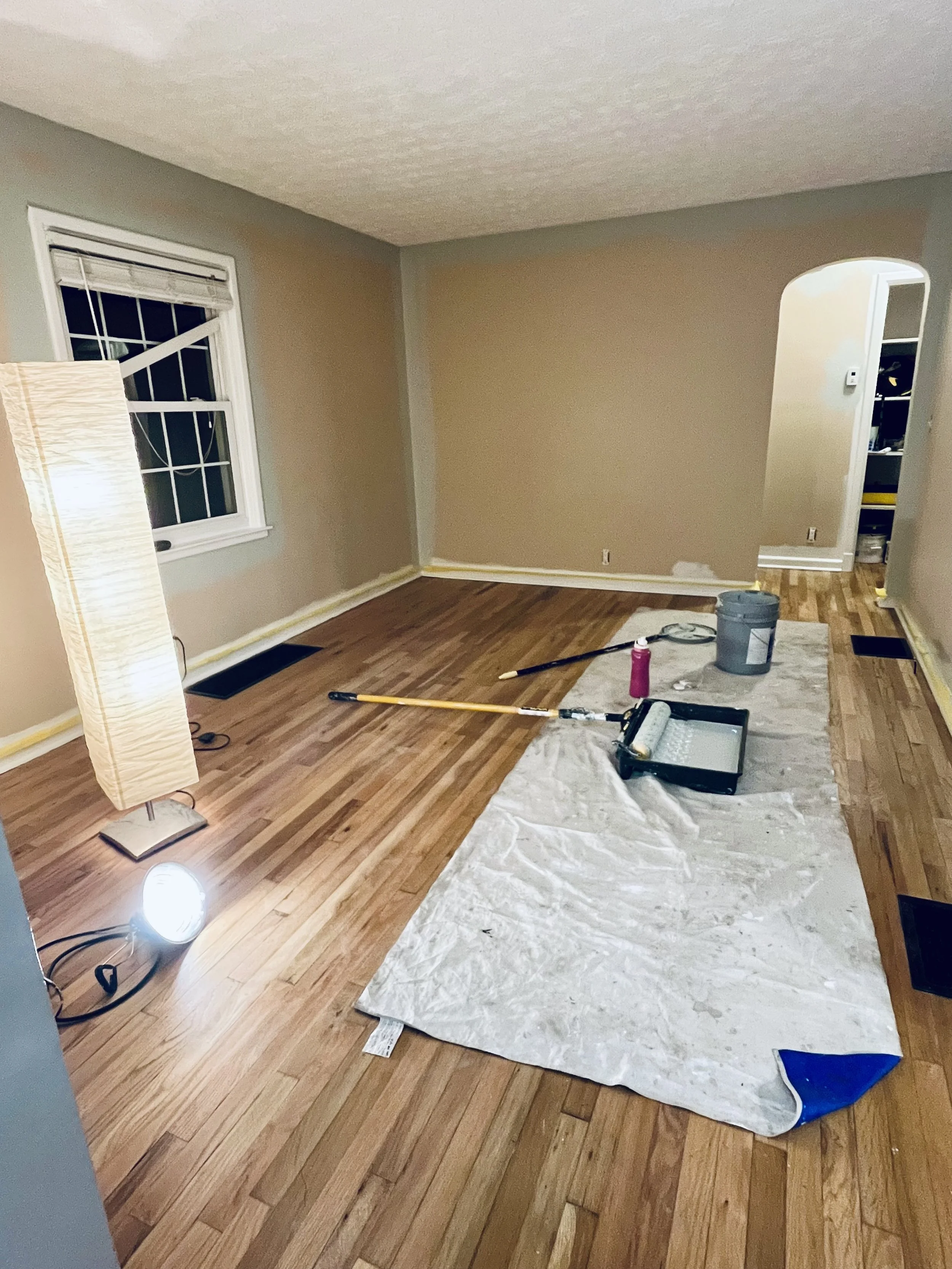 Room with hardwood floors being refinished, tools and a drop cloth on the floor, and a tall floor lamp in the corner.