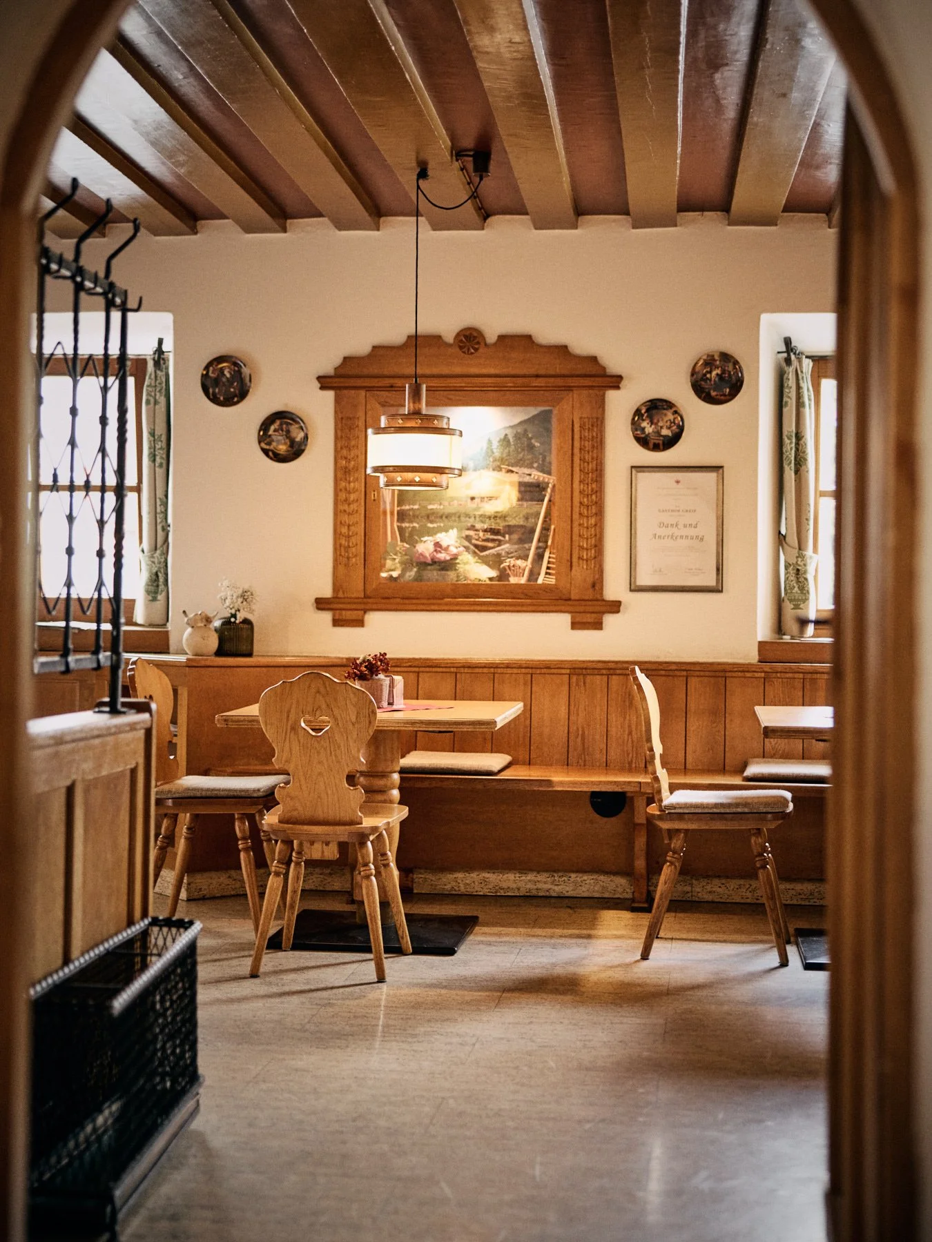 Innenraum eines rustikalen Restaurants mit Holztischen, Stühlen und Wandschmuck, Fenster mit Gardinen