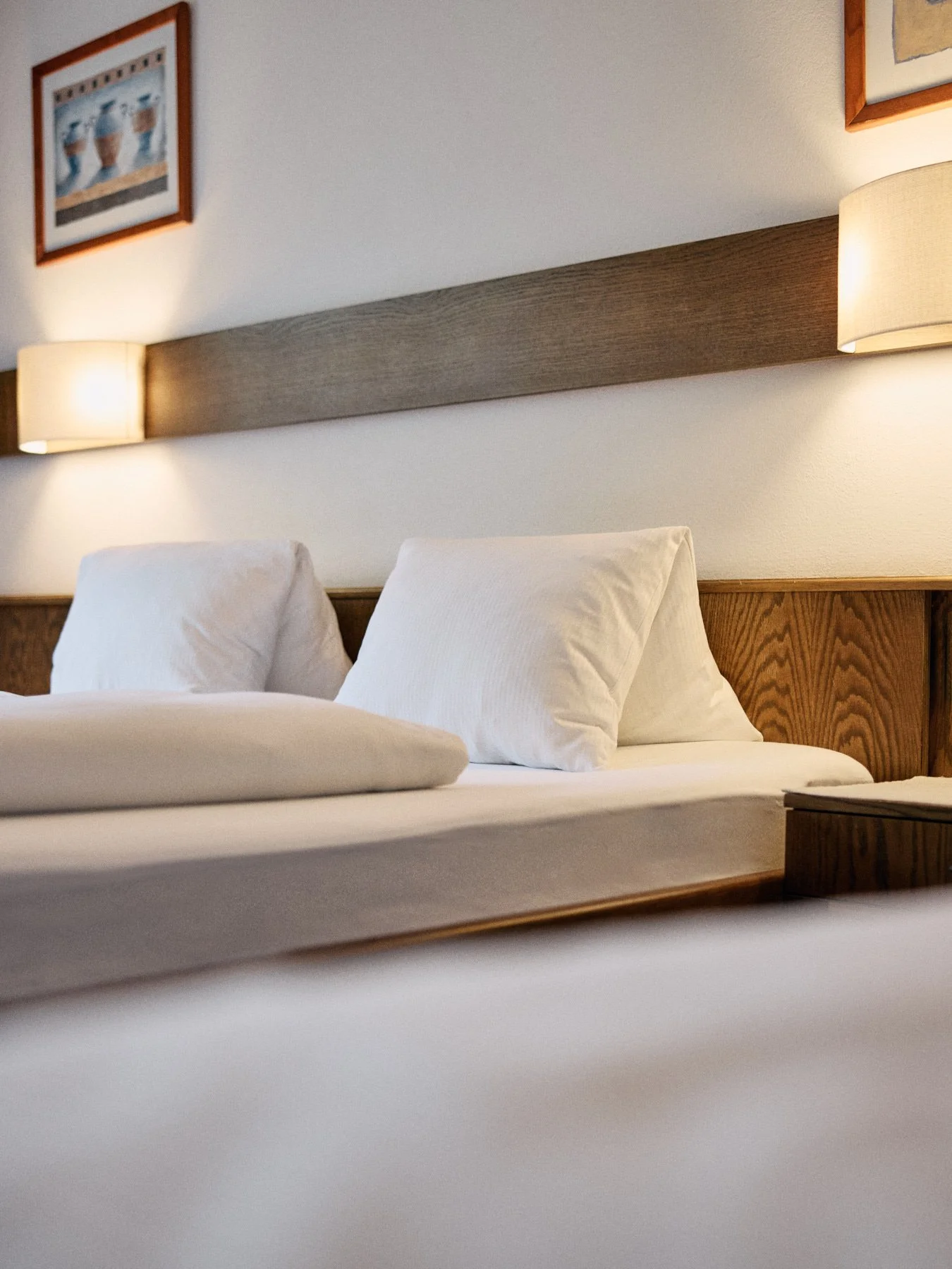 Bett mit weißen Kissen, Holzhintergrund, Wandlampen, Bilder an der Wand in einem Hotelzimmer
