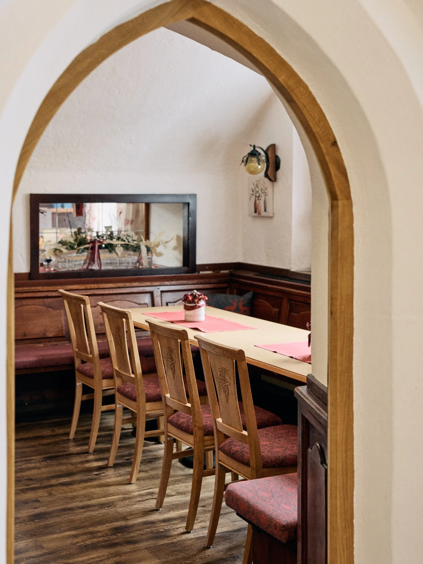 Ein gemütlicher Essraum mit Holztisch, Stühlen und Dekorationen, gesehen durch einen Holzrahmen einer Türöffnung.