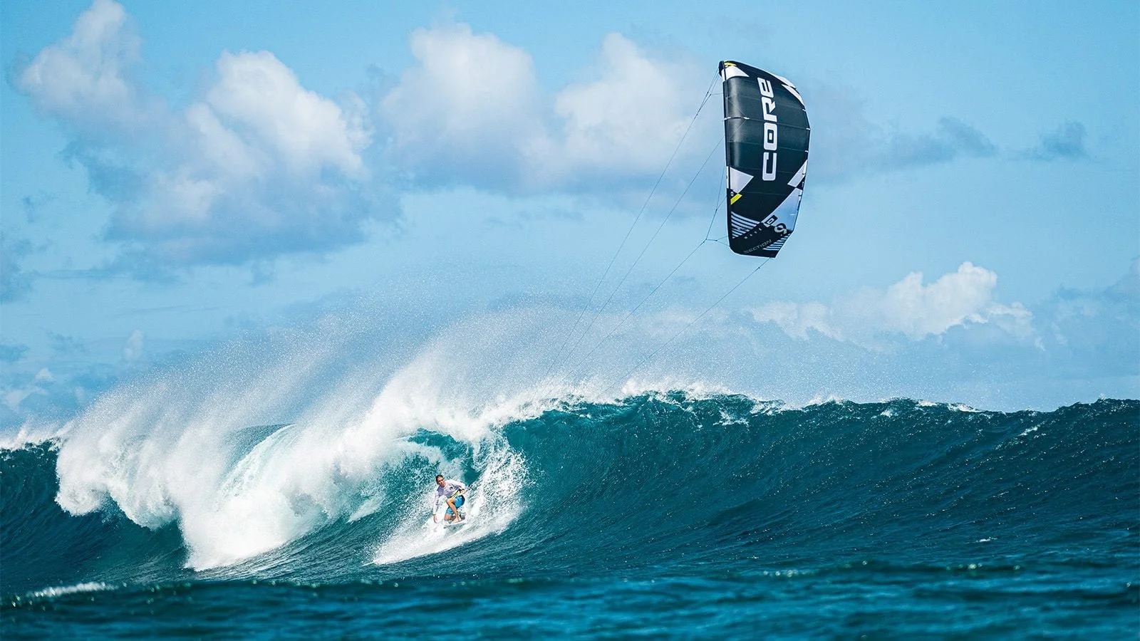 Kitesurfer riding a large ocean wave beneath a black CORE kite