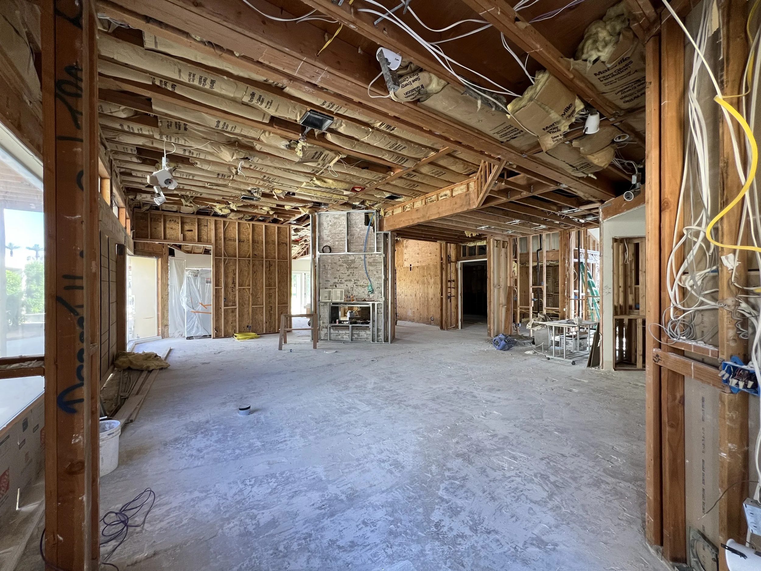 Interior of a house under construction with exposed wooden studs, wiring, insulation, and unfinished walls and ceiling.