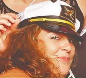 Woman with curly hair wearing a naval captain's hat, smiling
