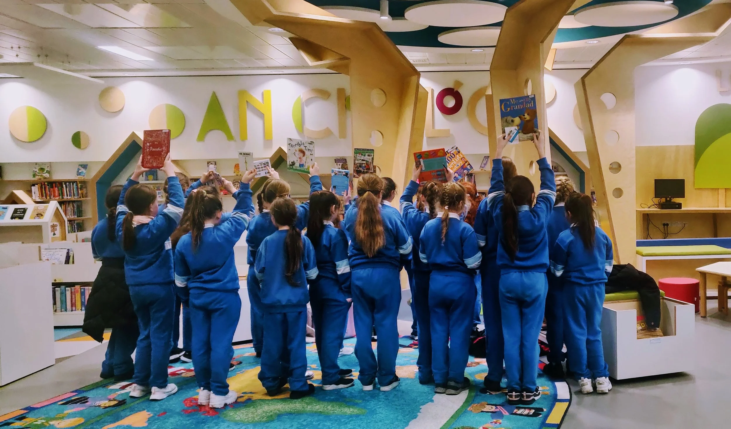 Group of children in blue school uniforms holding books in a colorful library or classroom