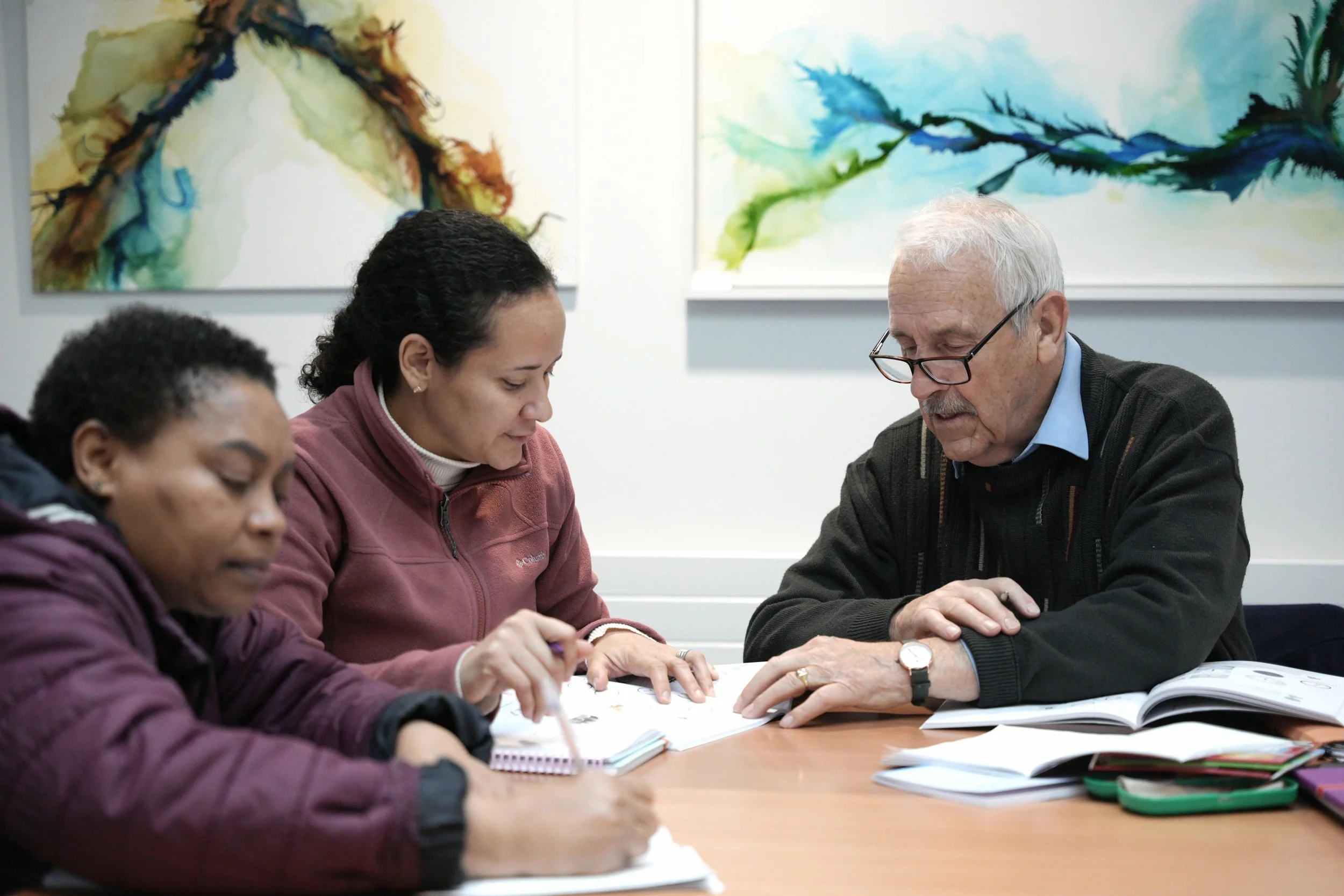 Three people sitting at a table in an art gallery, engaged in discussion and reviewing papers.