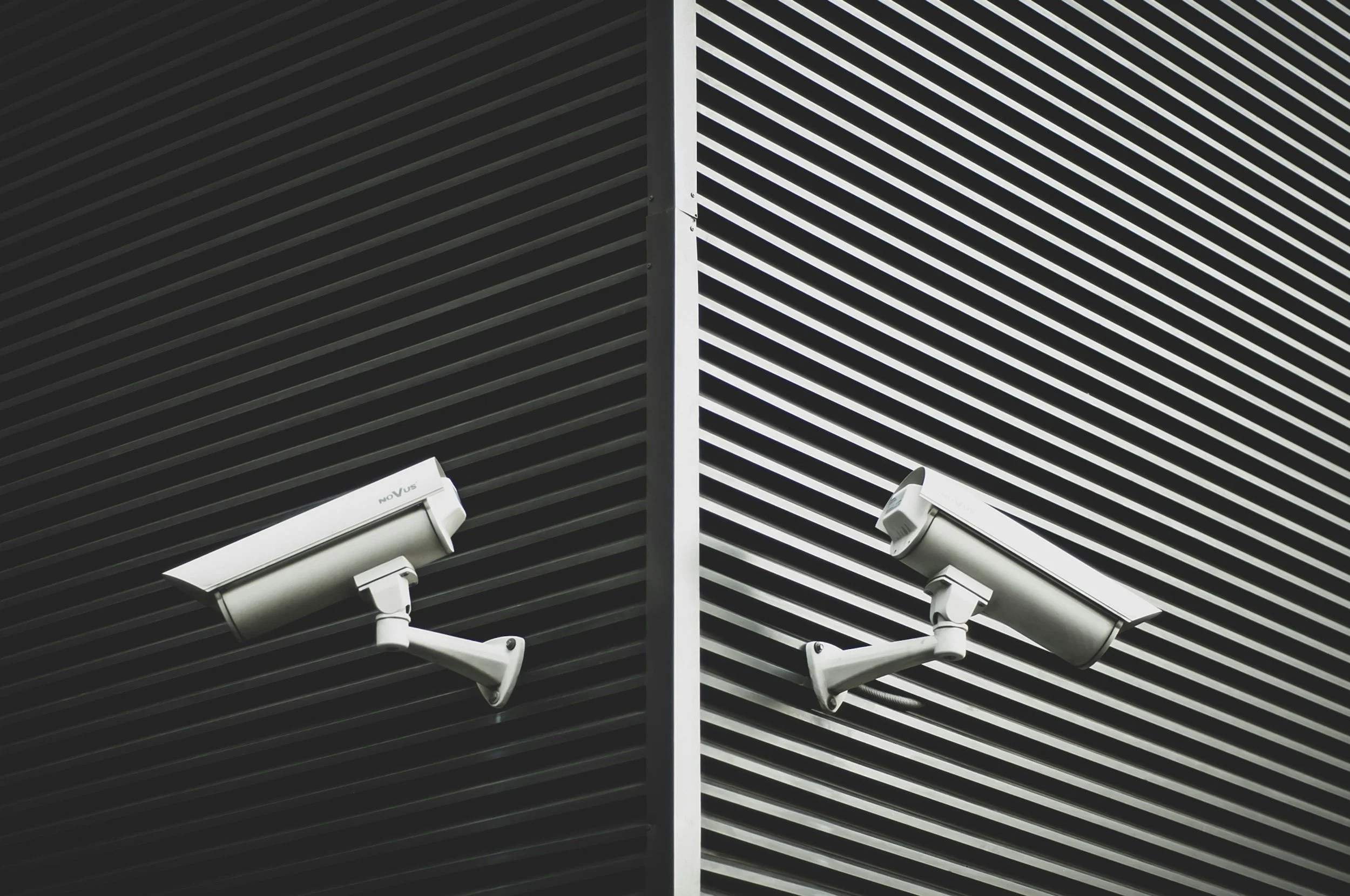 Close-up view of a building's exterior walls with diagonal slats, featuring two security cameras mounted on the bottom left side.