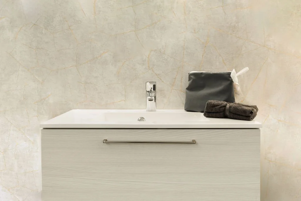 Valkoinen pesuallas, jossa on hana ja harjateline, taustalla vaaleankirjava seinä.