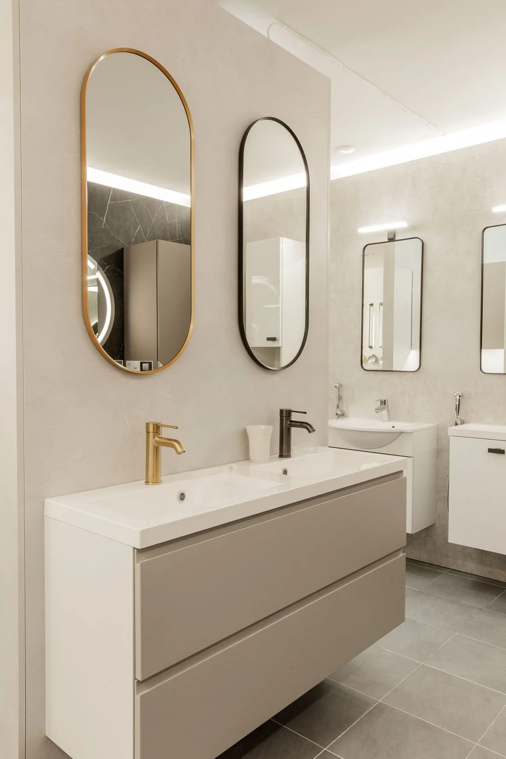 Kaksi kylpyhuoneenpeilikuvaa seinällä, valkoinen kakistilä, musta hana, peilikaappeja ja muita kylpyhuonetarvikkeita.