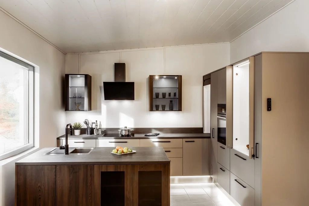 Keittiö avoimella suunnittelulla, jossa vaaleat alakaapit ja yläkaapit, keittiösaareke, ikkuna vasemmalla ja keittiötarvikkeita kuten kattila ja hedelmäkulho.