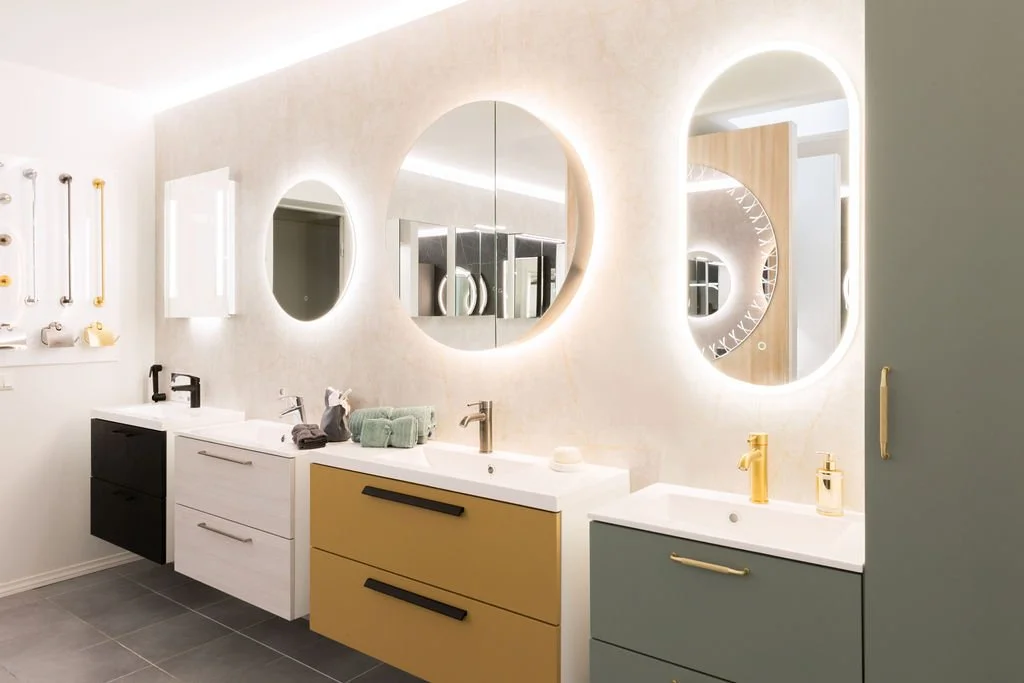 Tässä on moderni kylpyhuone, jossa on kolme kylpyhuoneallasunetta, kukin eri värinen ja varustettu suihkuilla ja peileillä, sekä koriste-esineitä ja pyyhkeitä.