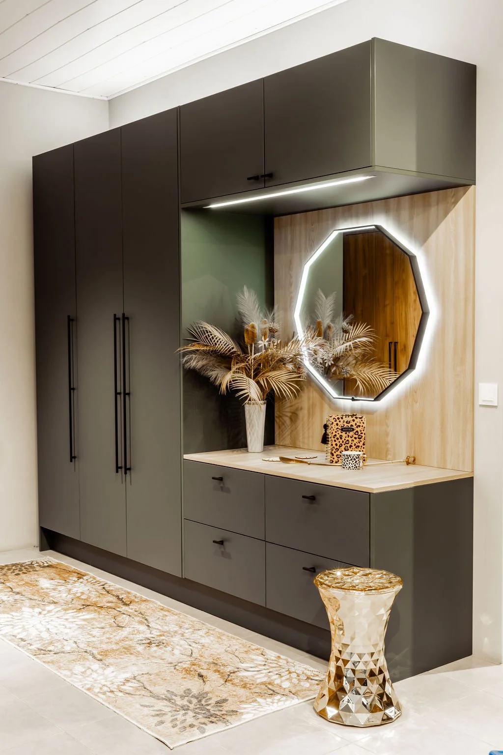 Moderni sisäänkäyntitarvikeyksenä mustat kaapistot, peili ja koriste-esineitä, kuten kukkakimppu, rasioita ja koriste-esineitä, ja pieni pöytä, kaikki sijoitettuna valkoiselle lattialle ja taustaseinälle, jossa on puukuvaus