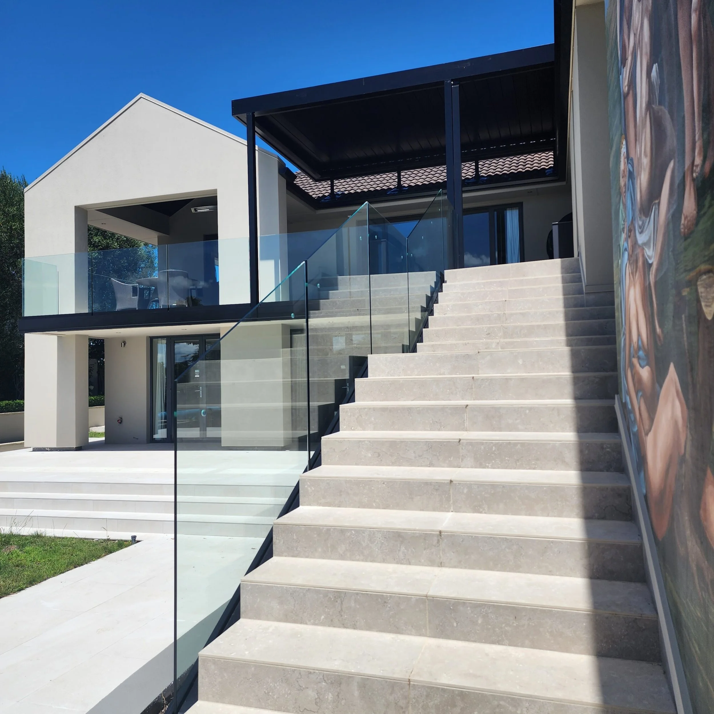 Modern house with outdoor stairs, glass railing, and a patio with outdoor furniture under a roof.