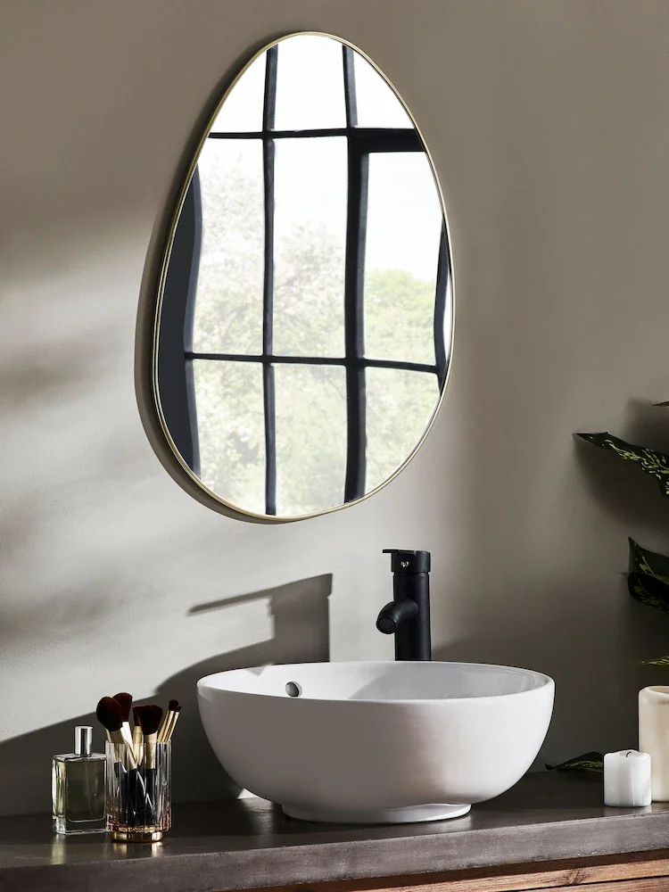 Bathroom vanity with a white oval vessel sink, black faucet, round mirror above, and toiletries like brushes, candle, and soap on the dark countertop.