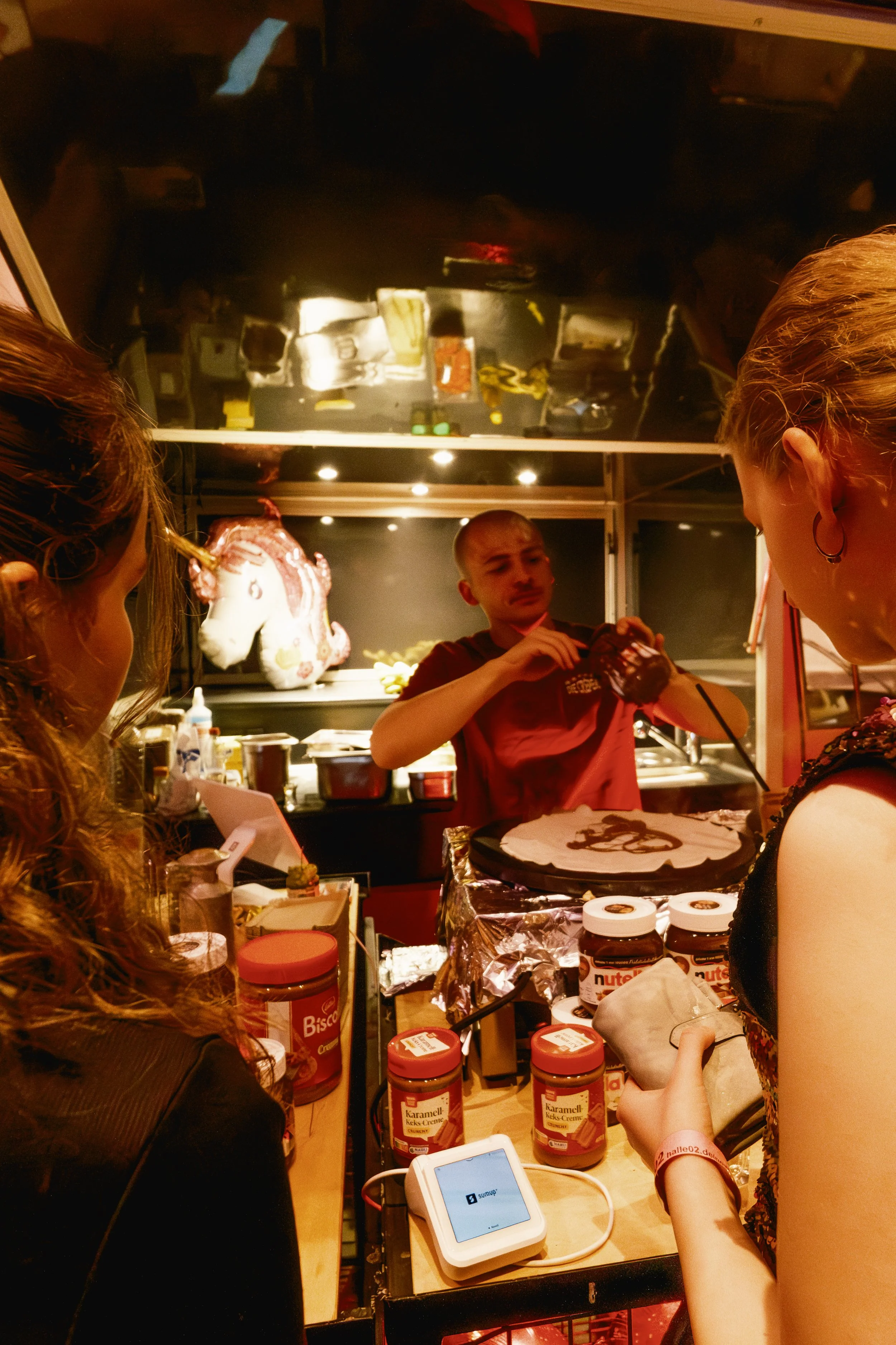 Eine Person beim Kuchenbacken hinter einer Theke, während zwei Frauen im Vordergrund zuschauen.