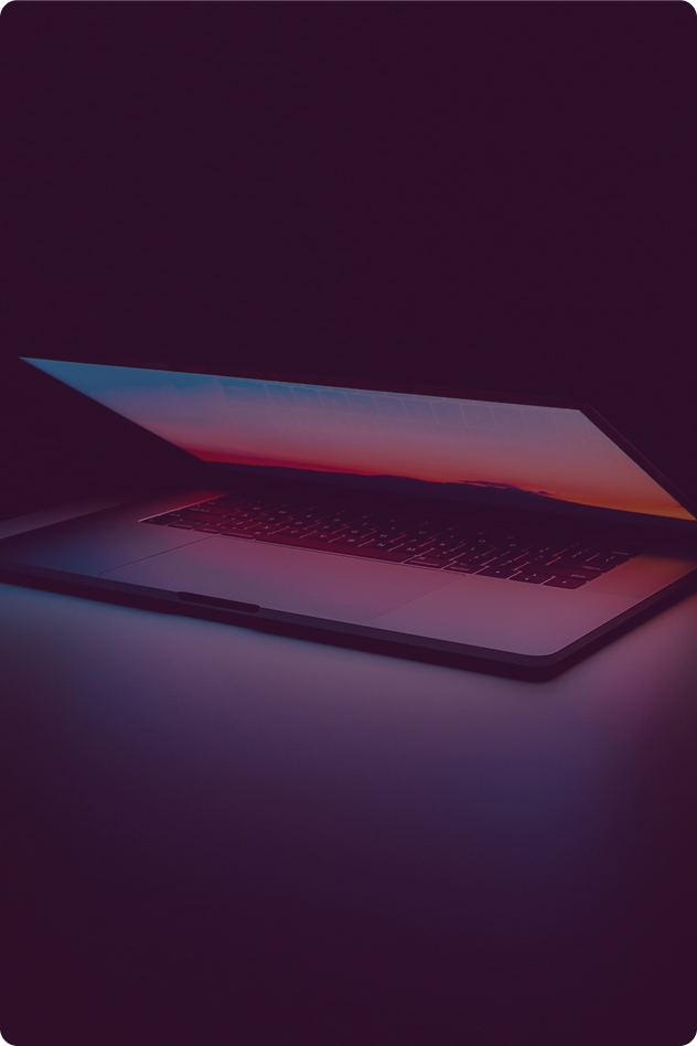 A laptop computer with a colorful sunset displayed on the screen, partially open in a dark environment.