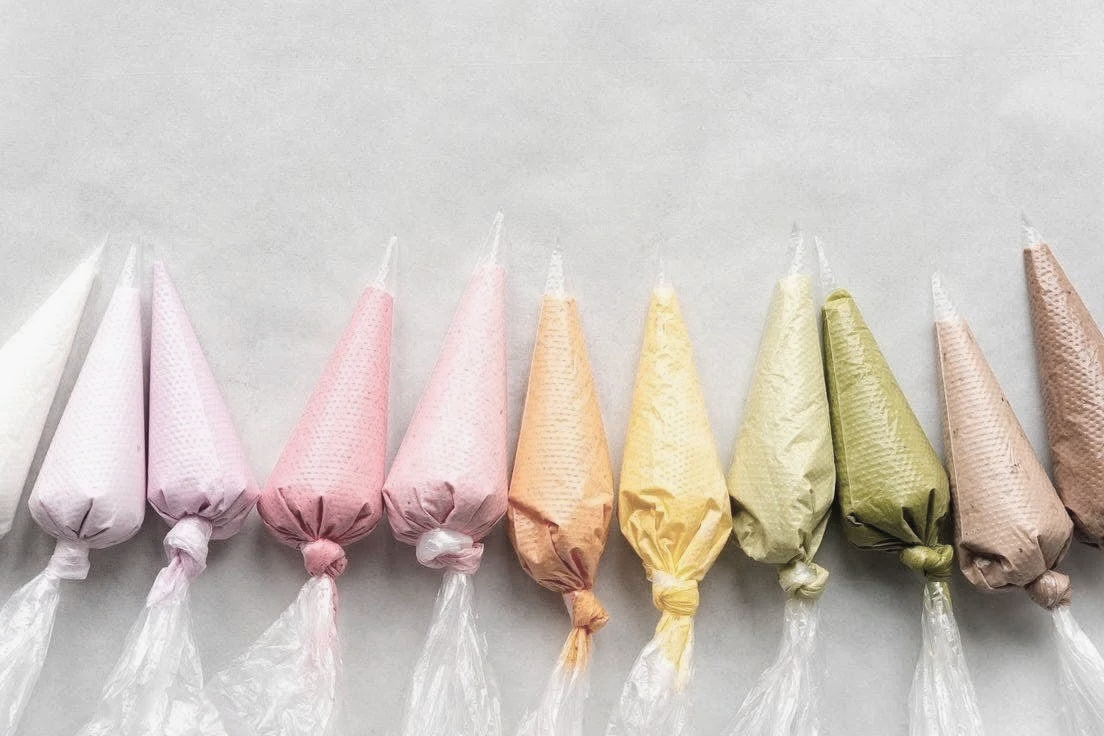 Eight pastel-colored frosted sugar cookies with clear wrapper ties, arranged in a row on a light gray surface.