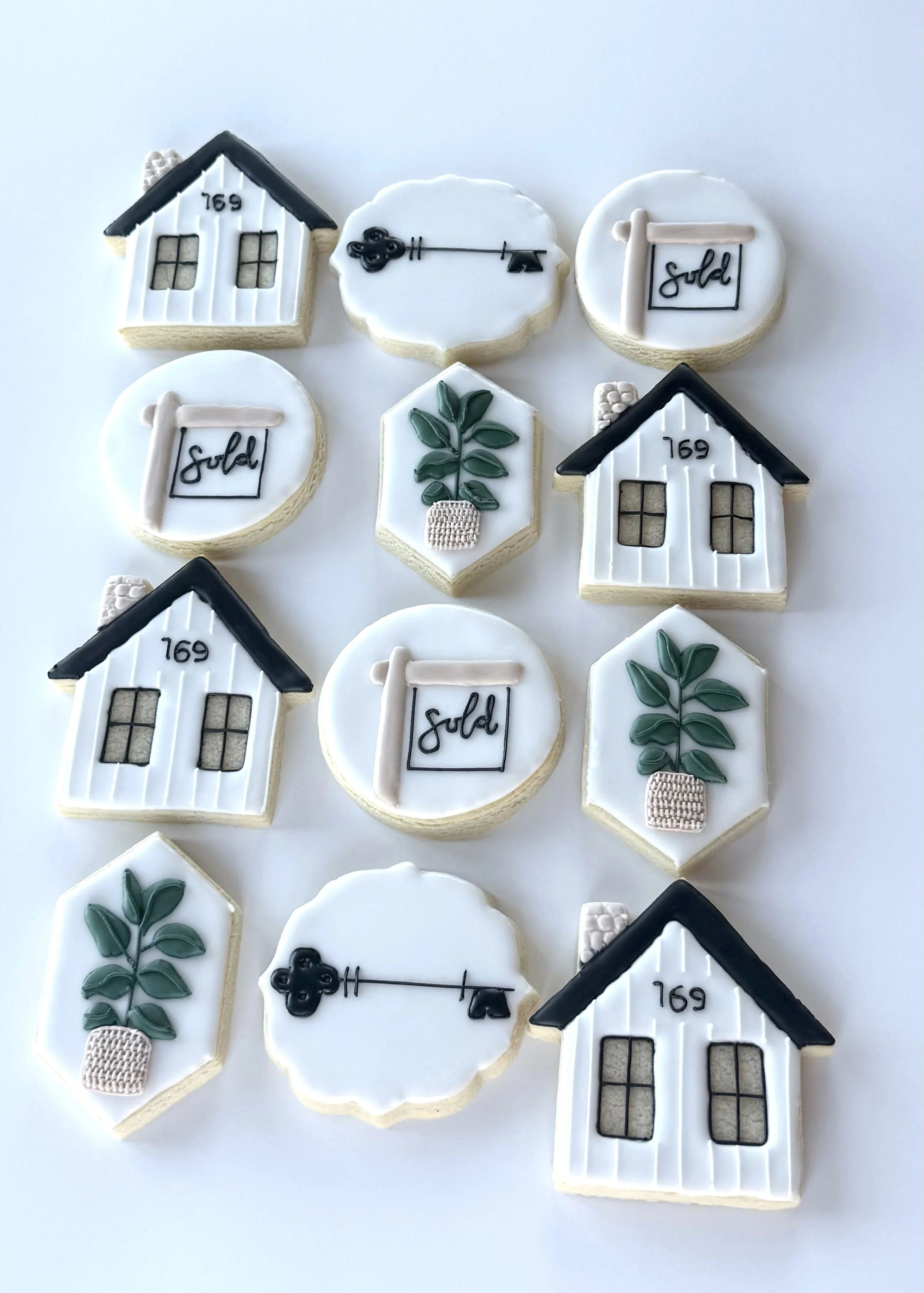 Assorted decorative cookies with house, key, sold sign, and plant designs on a white background.