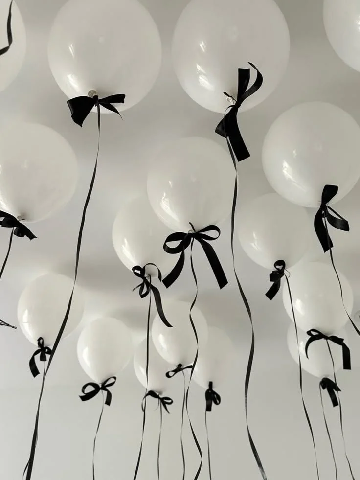 White balloons tied with black ribbons floating against a white ceiling.