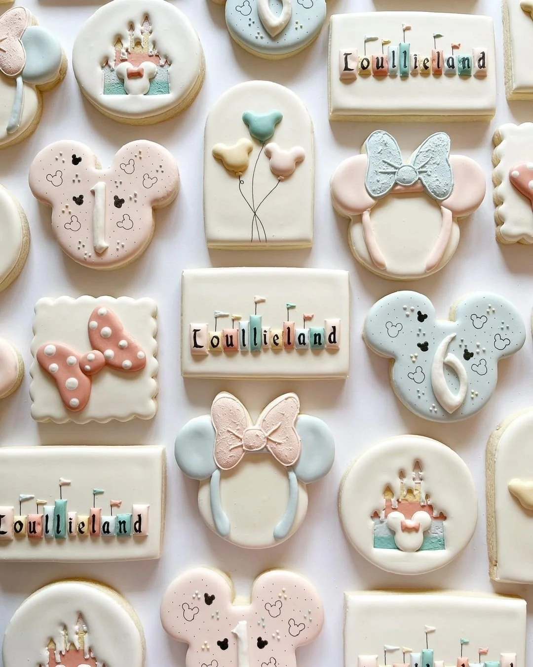 Assorted pastel-colored cookies with Disney and birthday themes, including Mickey Mouse ears, bows, balloons, and birthday cakes with the word 'Loulieland' spelled out in colorful letter blocks.
