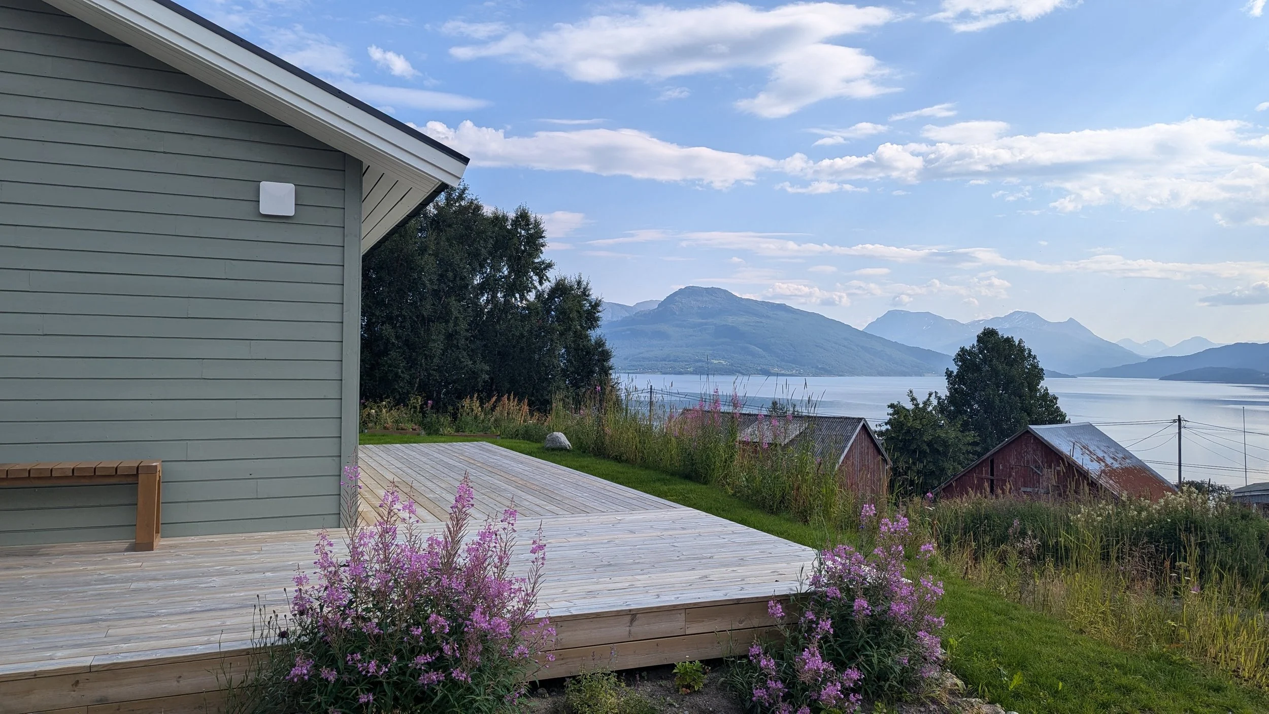 Utsikt over Astafjorden med fjell i bakgrunnen, en terrasse med blomster og en del av et hus i forgrunnen.