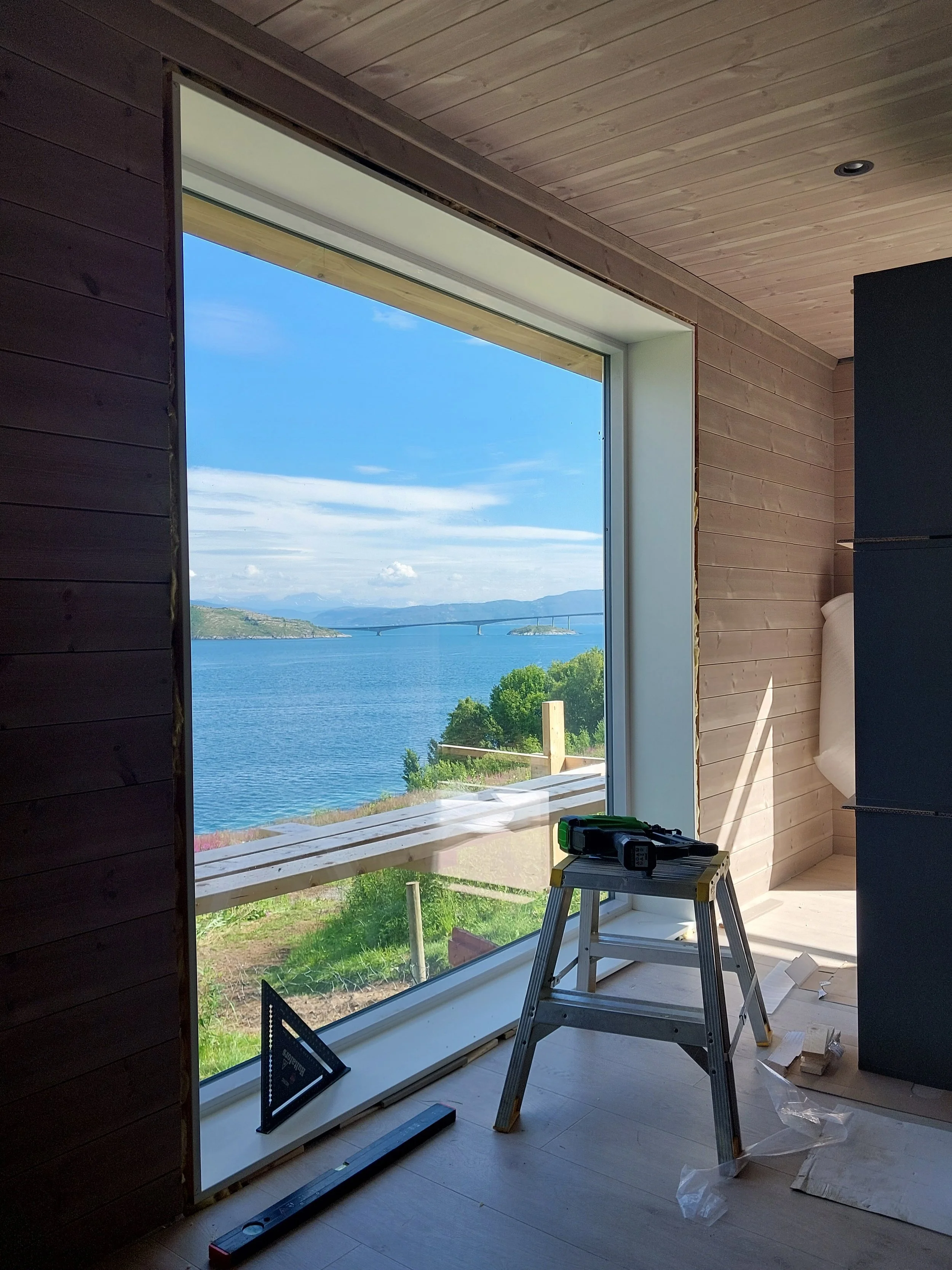 Innendørs utsikt mot et stort vindu med utsikt over sjø. Innvendig oppussing pågår.