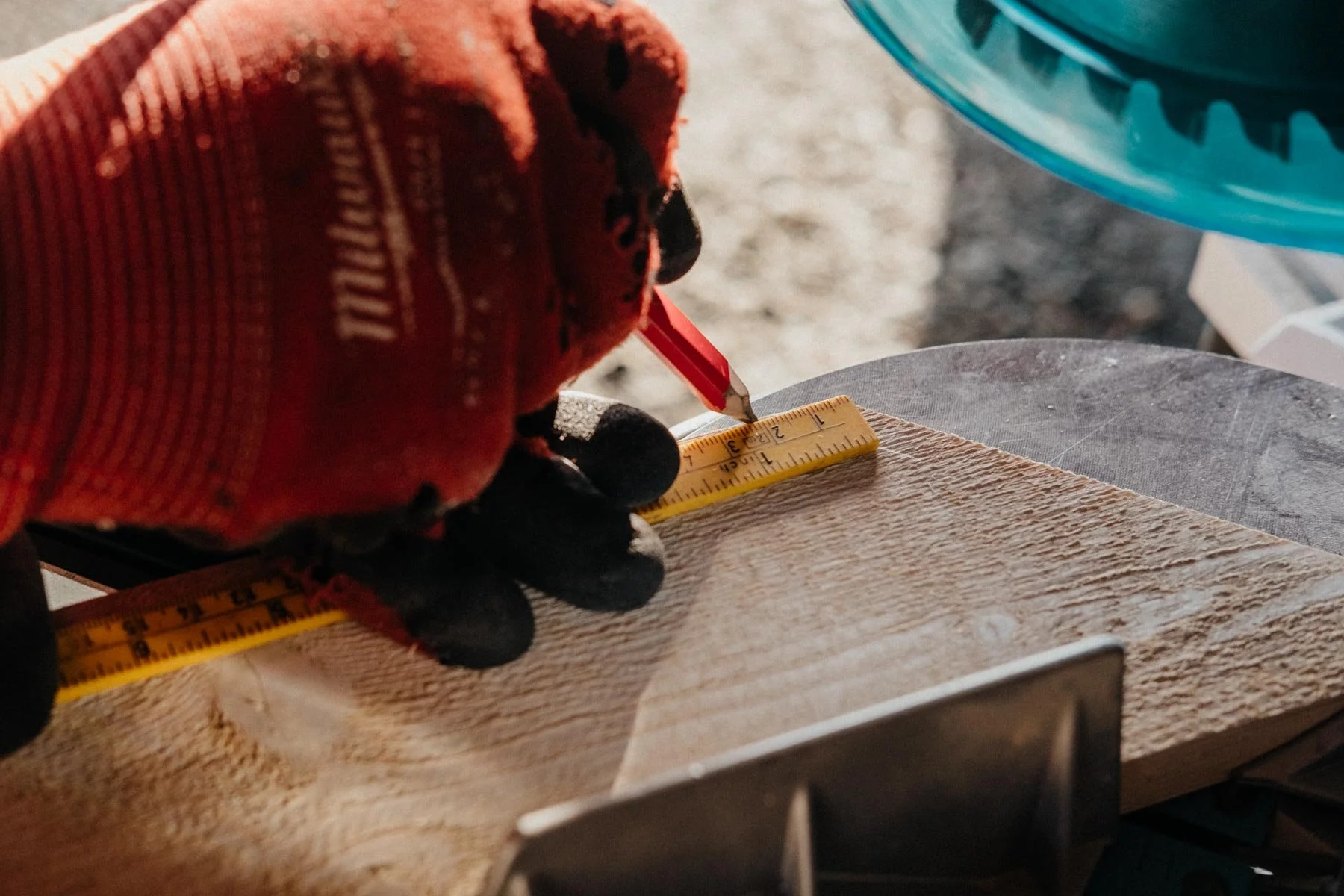 En person måler en treskive med et målebånd og et rutenett, iført røde og svarte arbeidshansker.