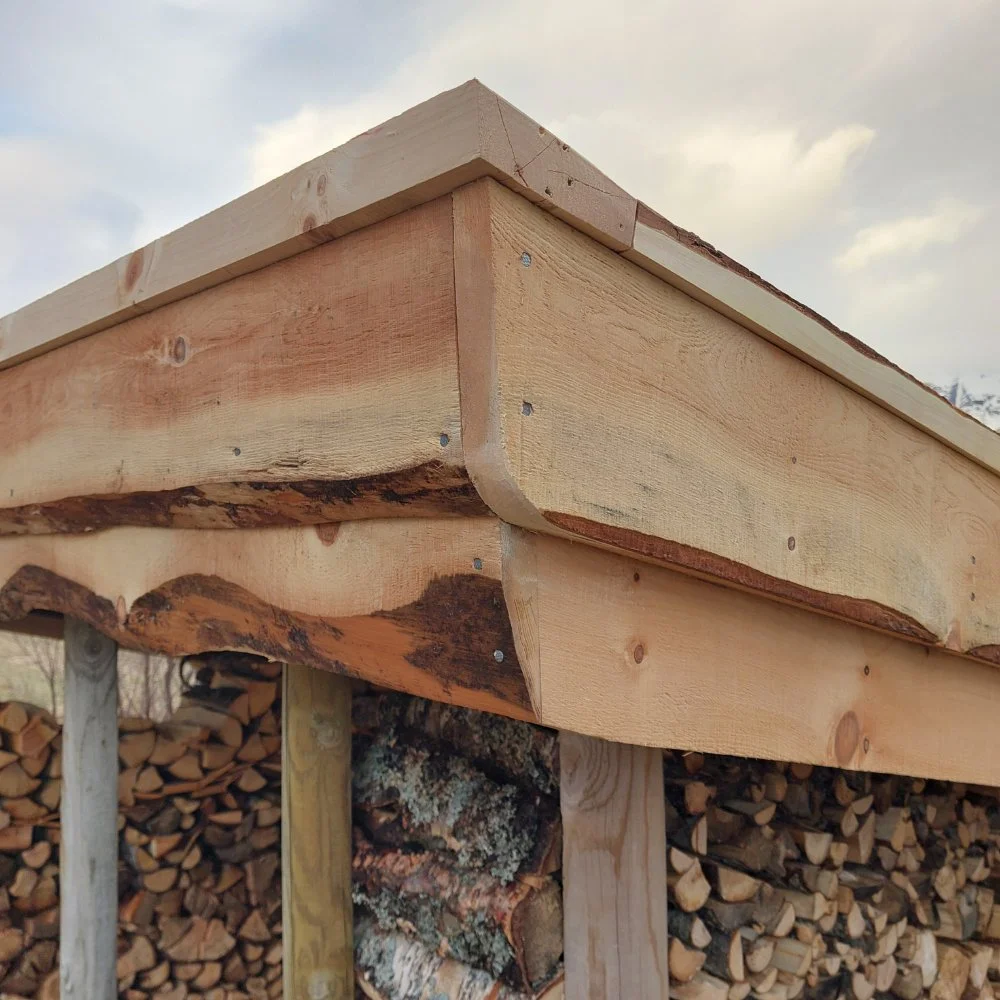 Et nært bilde av en hjørne av en tretak, med vedhaug i bakgrunnen.