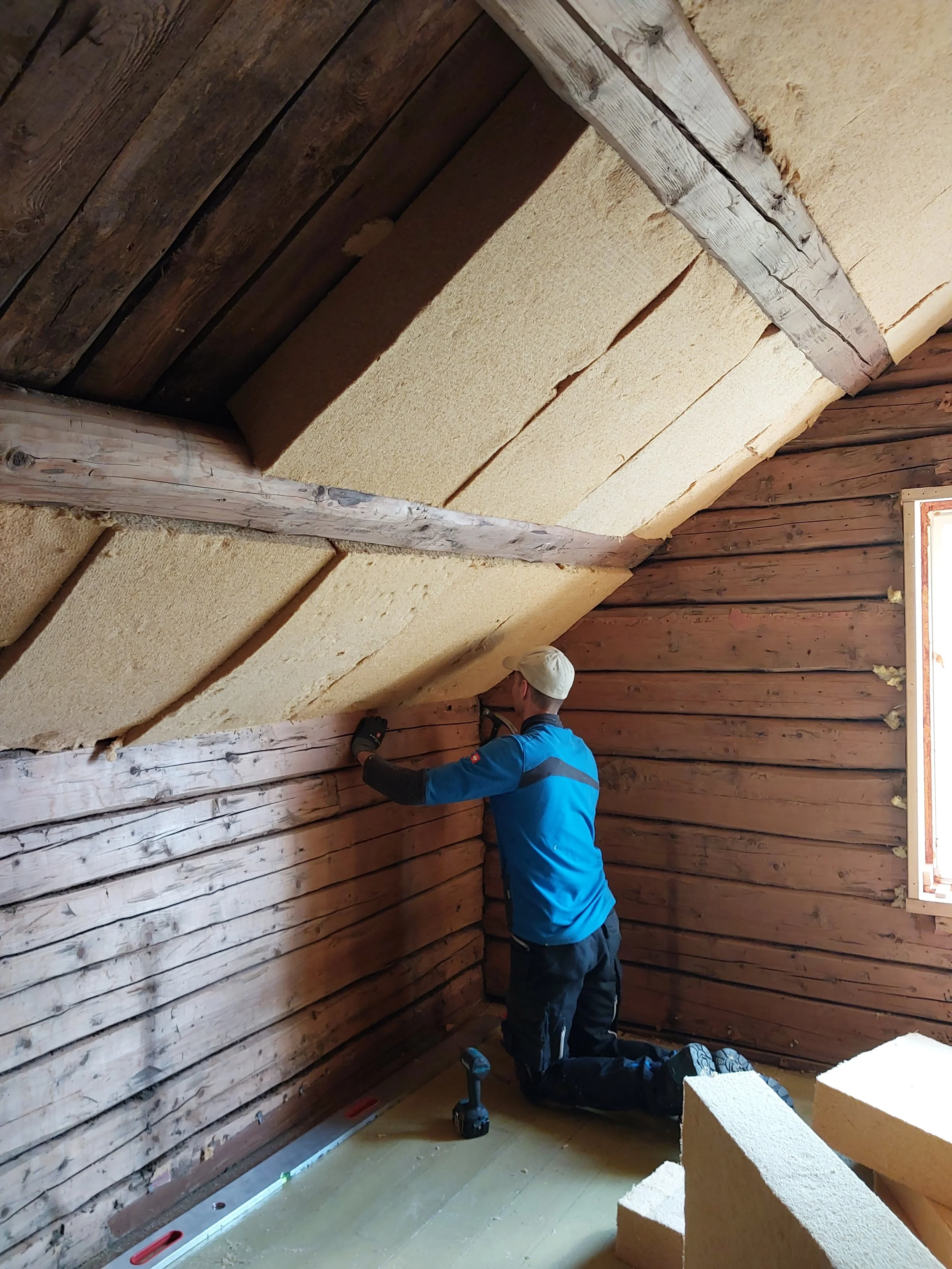 En person installerer isolasjon i øvre etasjen i et rom med trevegger og skråtak.