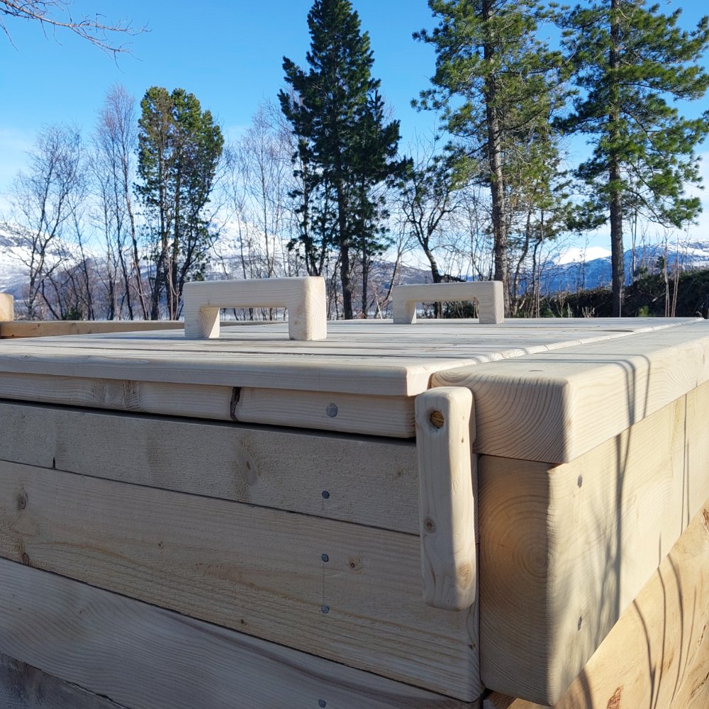 Nærbilde av et ferdig konstruert kompostbinge med håndtak, plassert utendørs med trær og fjell i bakgrunnen.