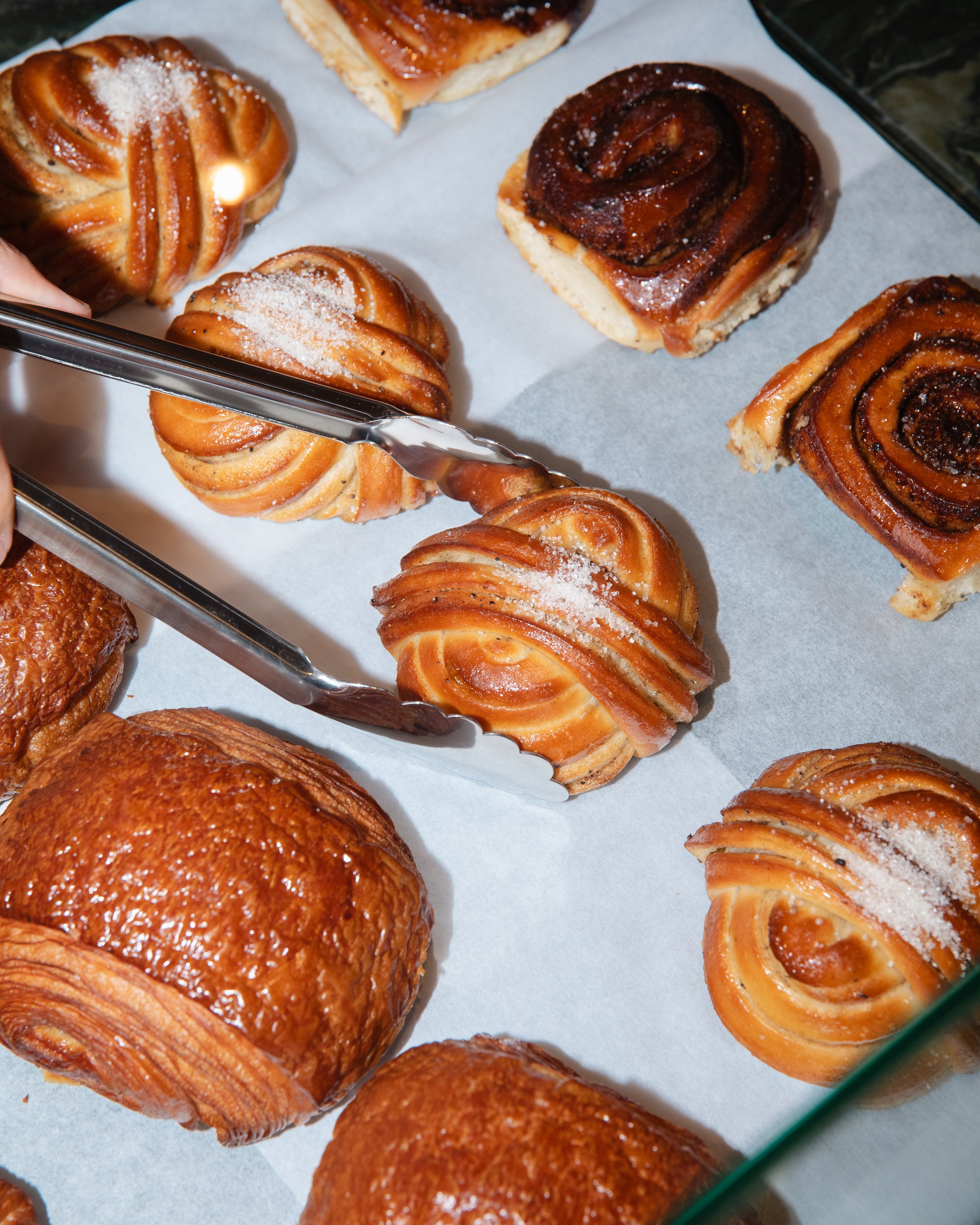 Billedet viser forskelligt bagværk, herunder kardemommesnurrer, kanelsnegle og pain au chocolat, lagt på et stykke bagepapir.