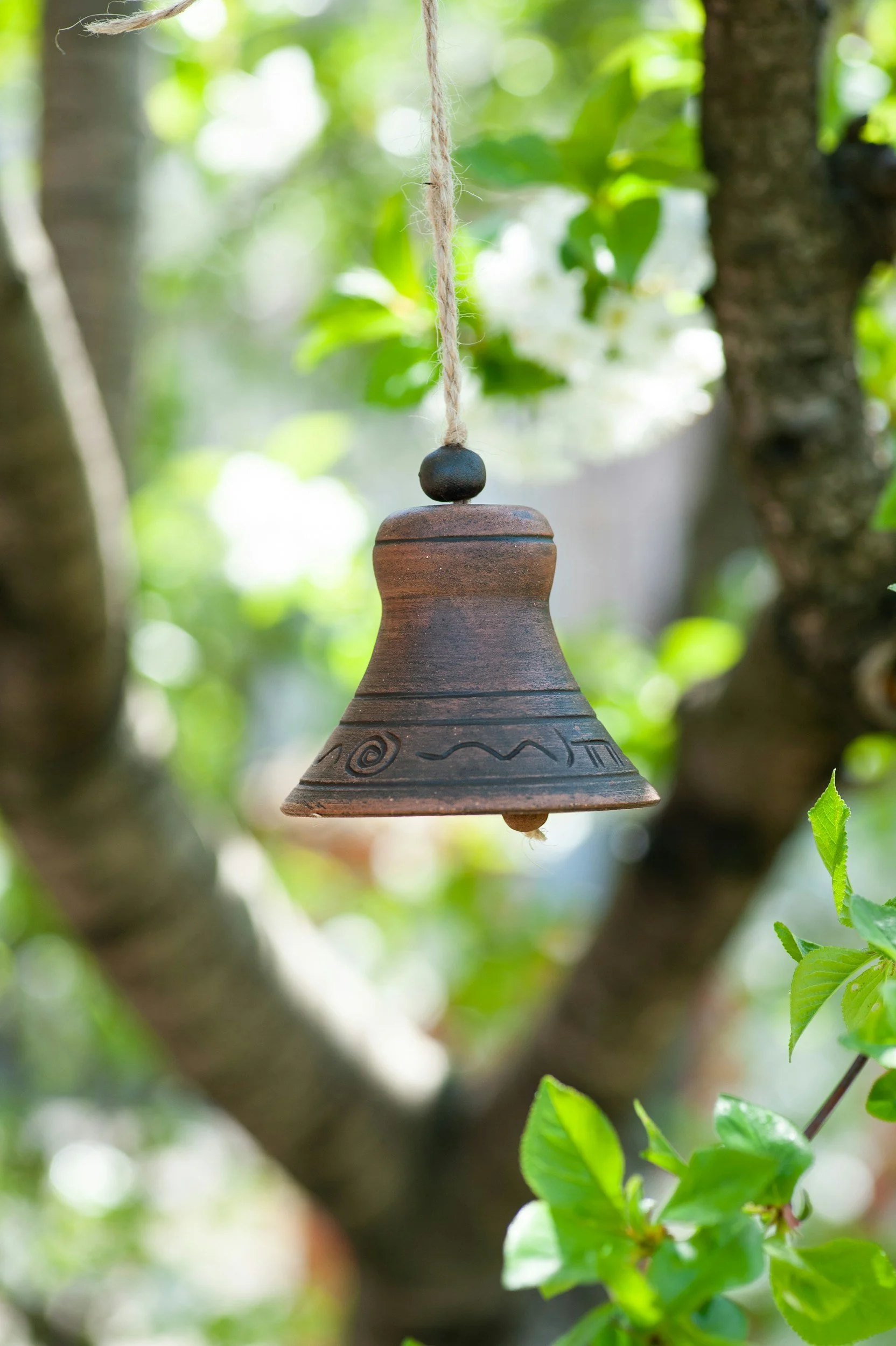 A small wooden bell hanging from a tree branch with green leaves in the background.