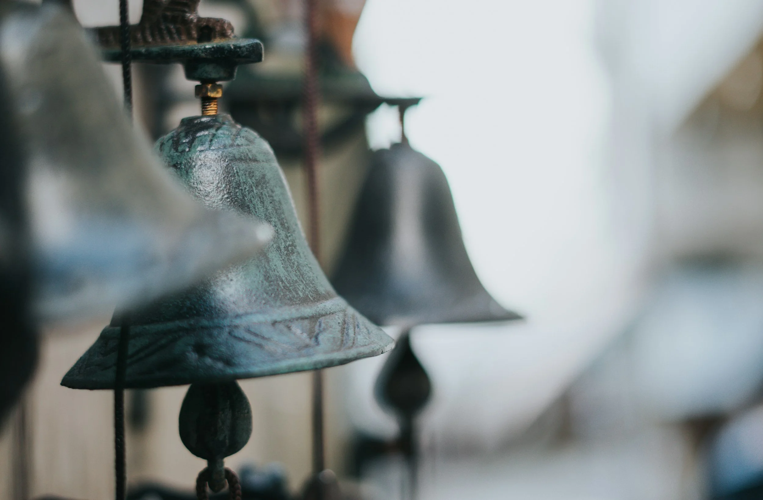 Close-up of several old, metallic church bells hanging on a wall.