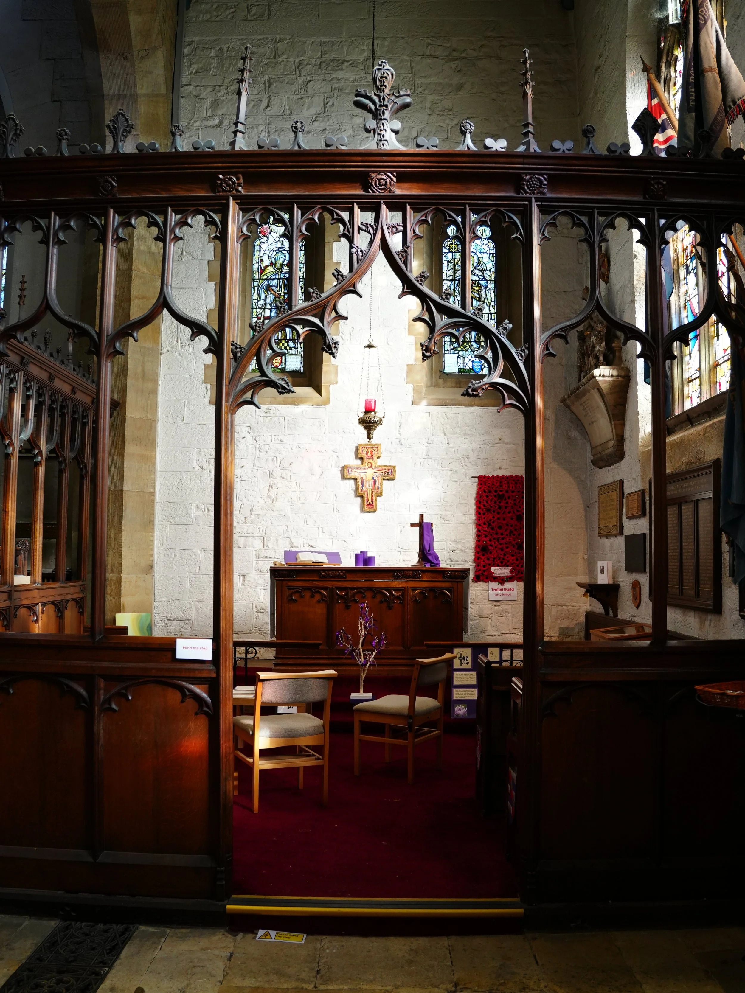 Interior of a small church or chapel with wooden altar, purple cloth, chairs, stained glass windows, and religious symbols.