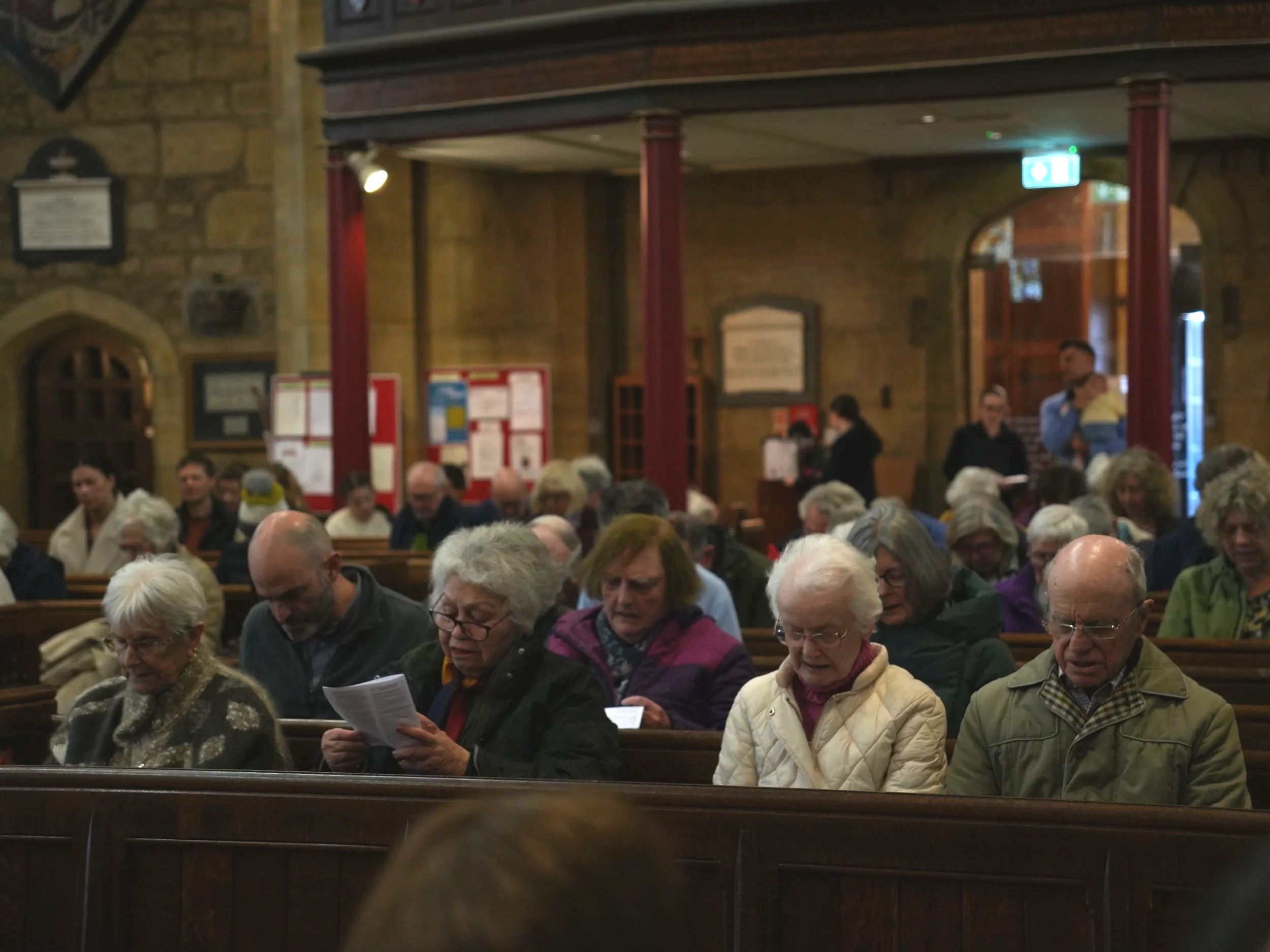 A group of elderly people sitting in pews inside a church, reading or praying during a service.