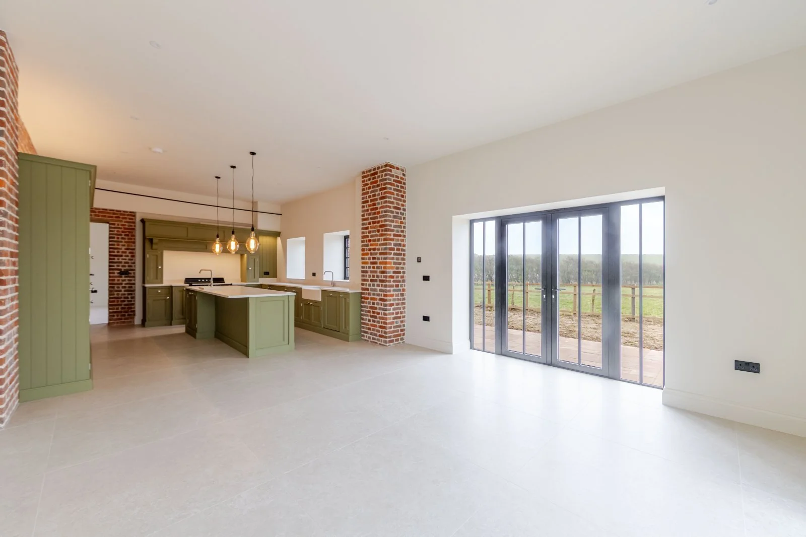 Open-concept kitchen with green cabinets, brick accents, large sliding glass doors, and natural light.