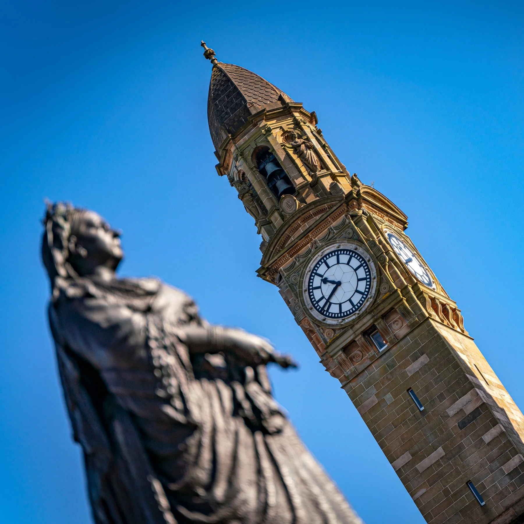Clock tower with a statue in the foreground against a blue sky.