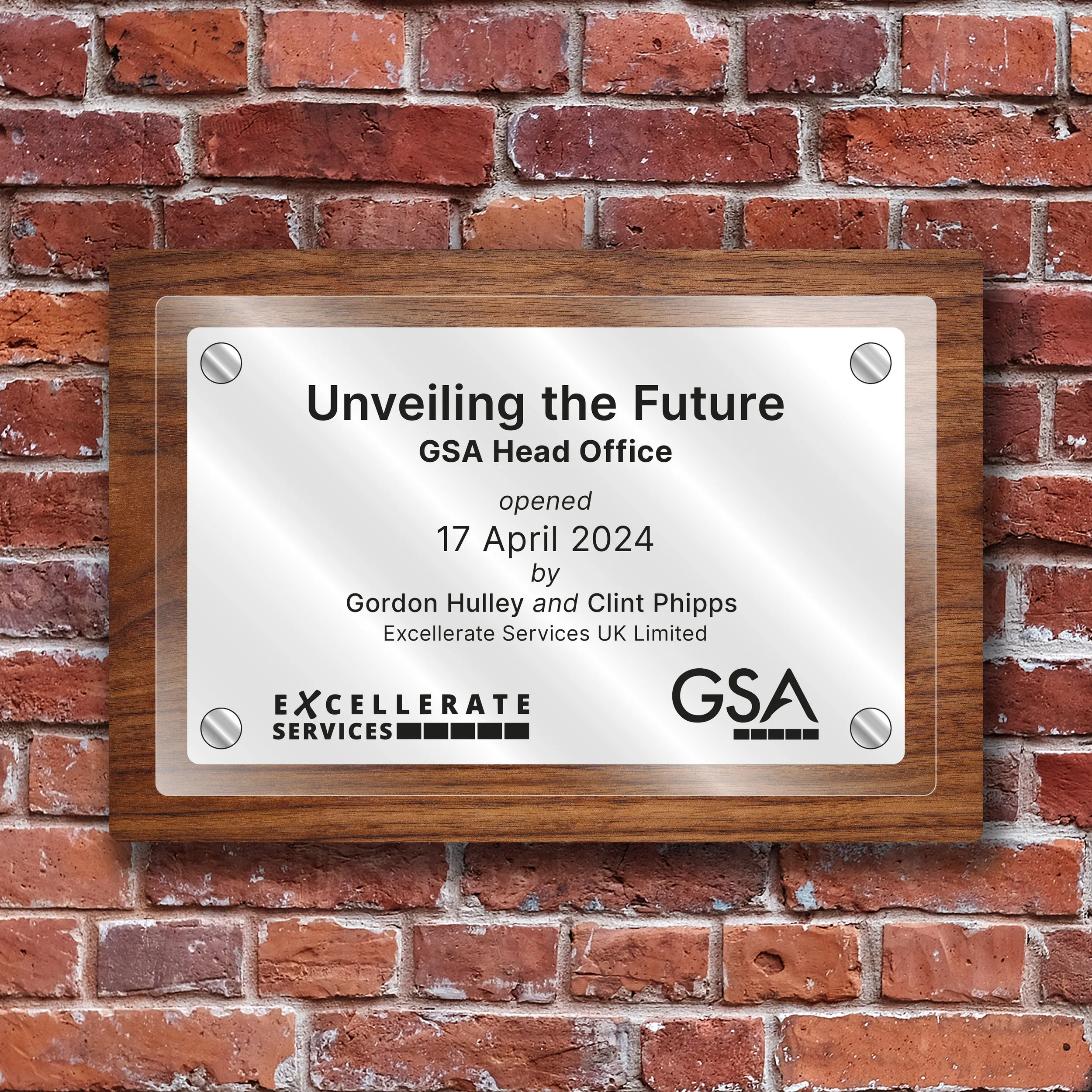 A plaque mounted on a brick wall, announcing the opening of the GSA Head Office on April 17, 2024, by Gordon Hulley and Clint Phipps, with logos of Excellerate Services UK Limited and GSA.